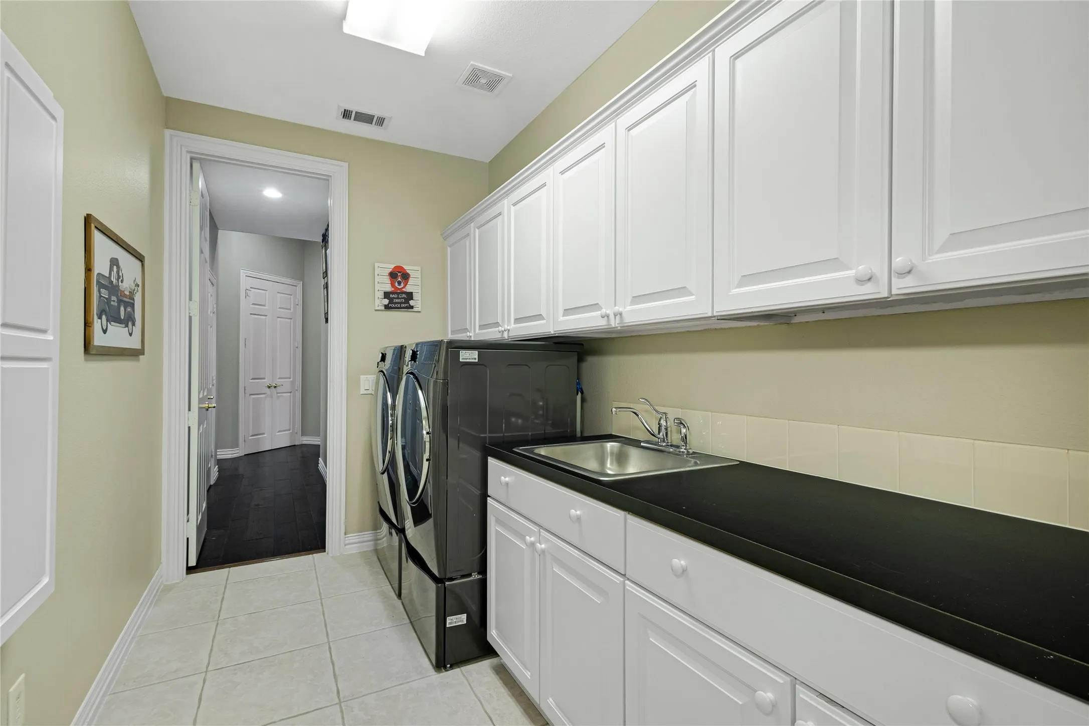 Utility room with tiled flooring, white cabinetry, dark countertops, and a stainless steel sink