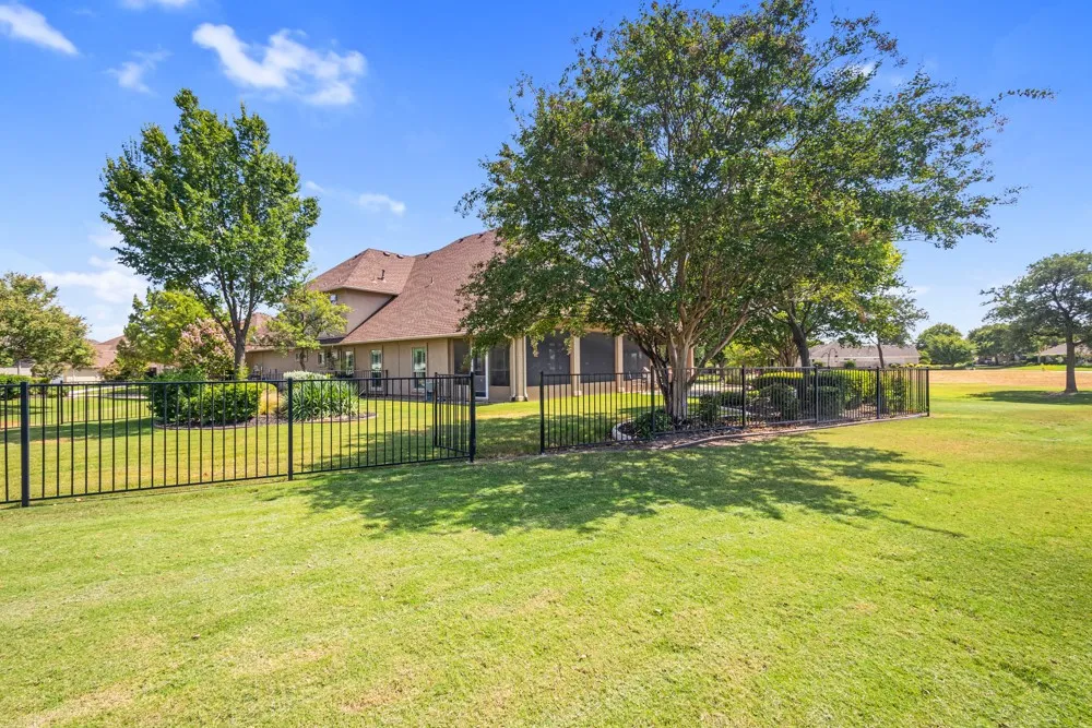 Expansive lawn area with mature trees, black metal fencing, and a landscaped perimeter
