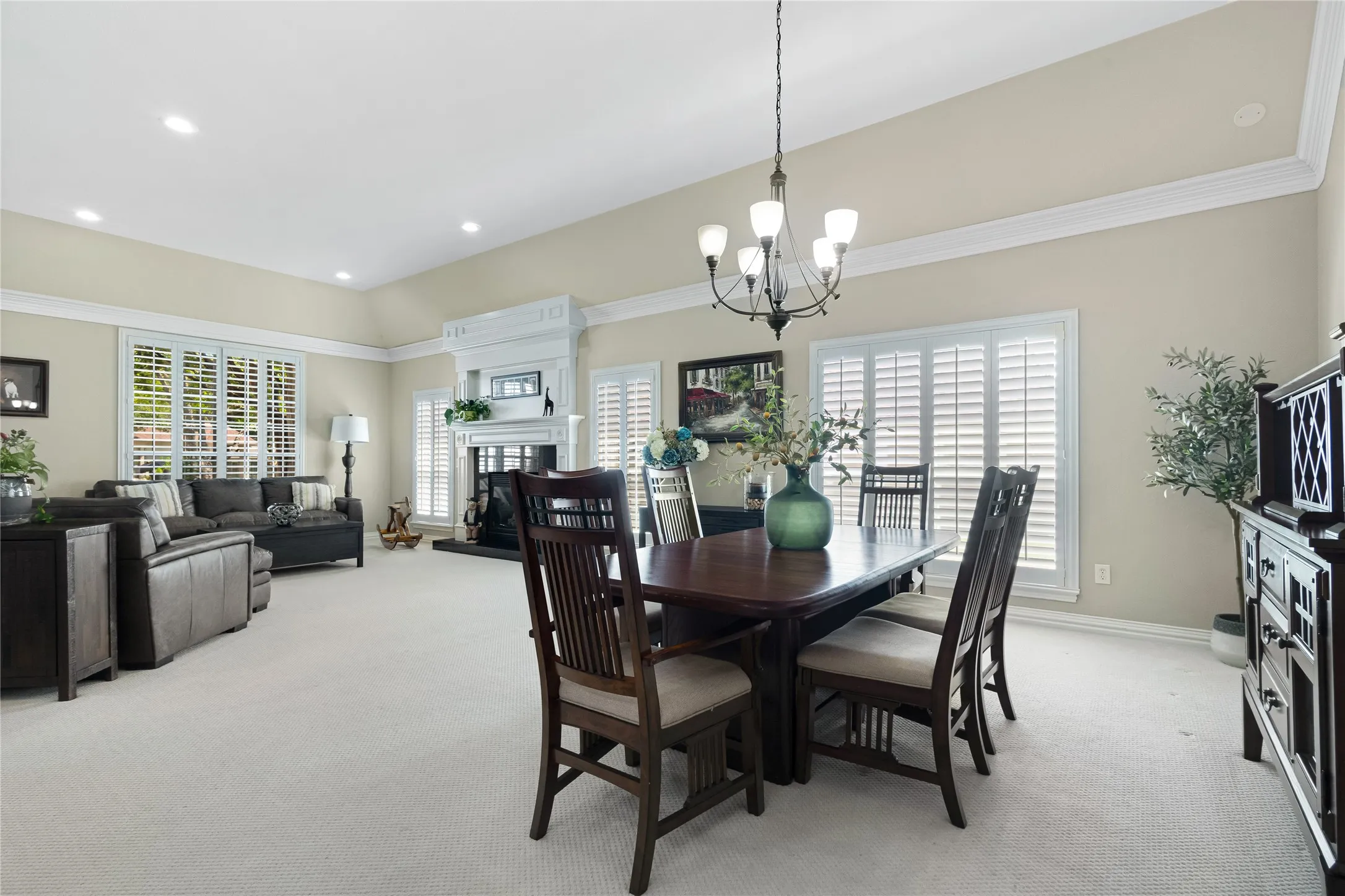 Vaulted ceiling with recessed lighting, crown molding, white plantation shutters, and a classic fireplace with a white mantel