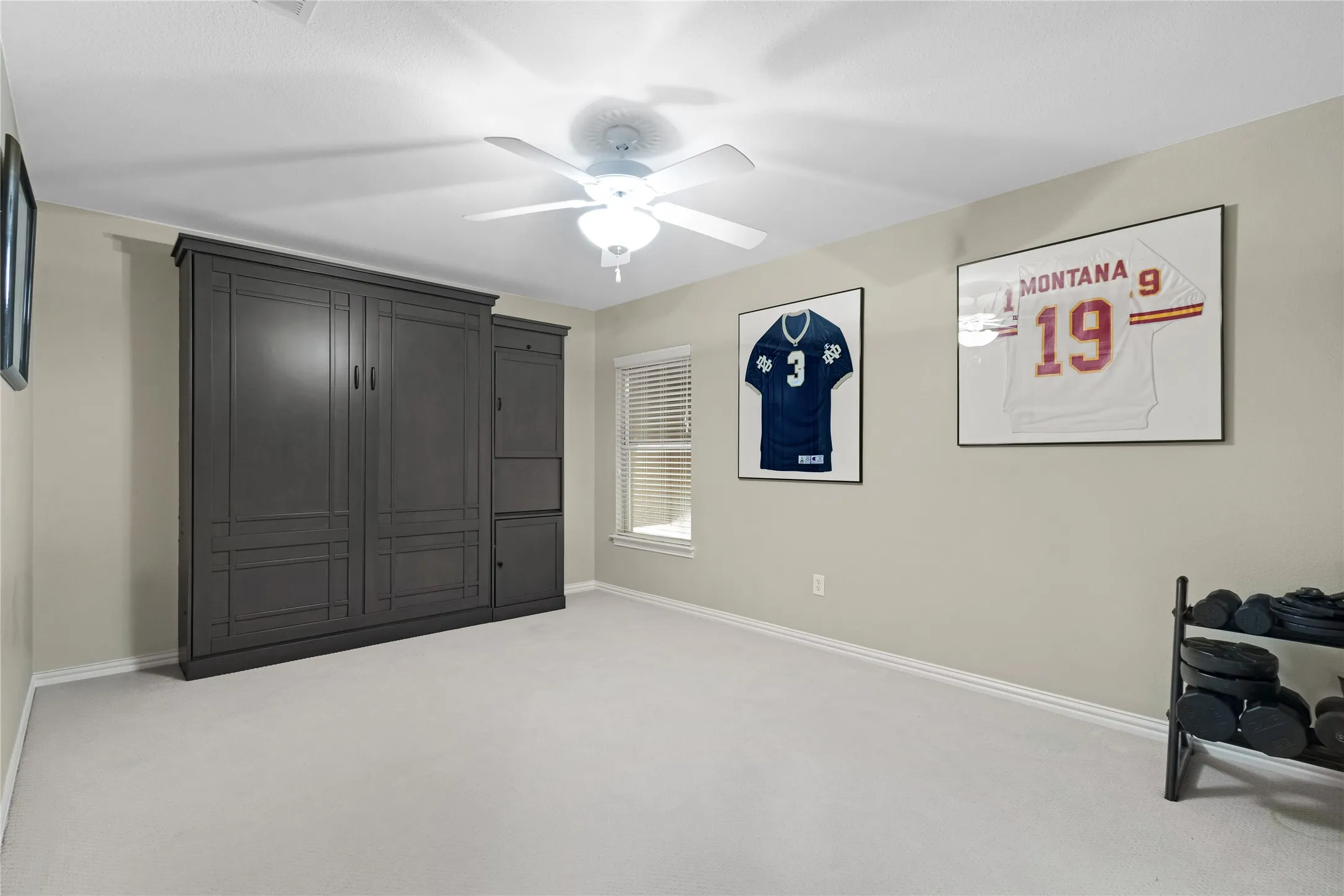 Built-in cabinetry with paneled doors, neutral wall tones, window with blinds, and ceiling fan