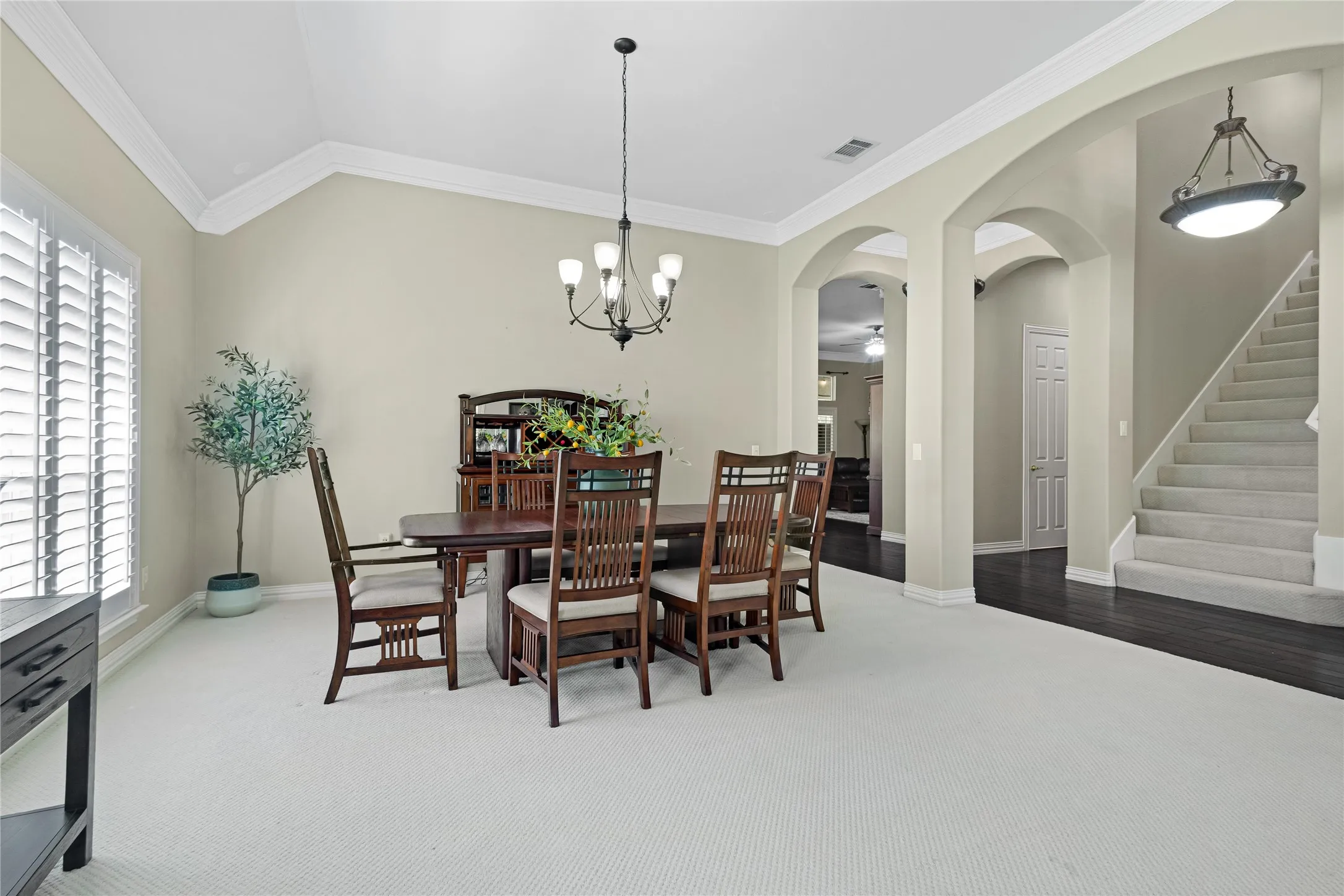 Vaulted ceiling, crown molding, plantation shutters, arched doorways, and dark wood-finish flooring