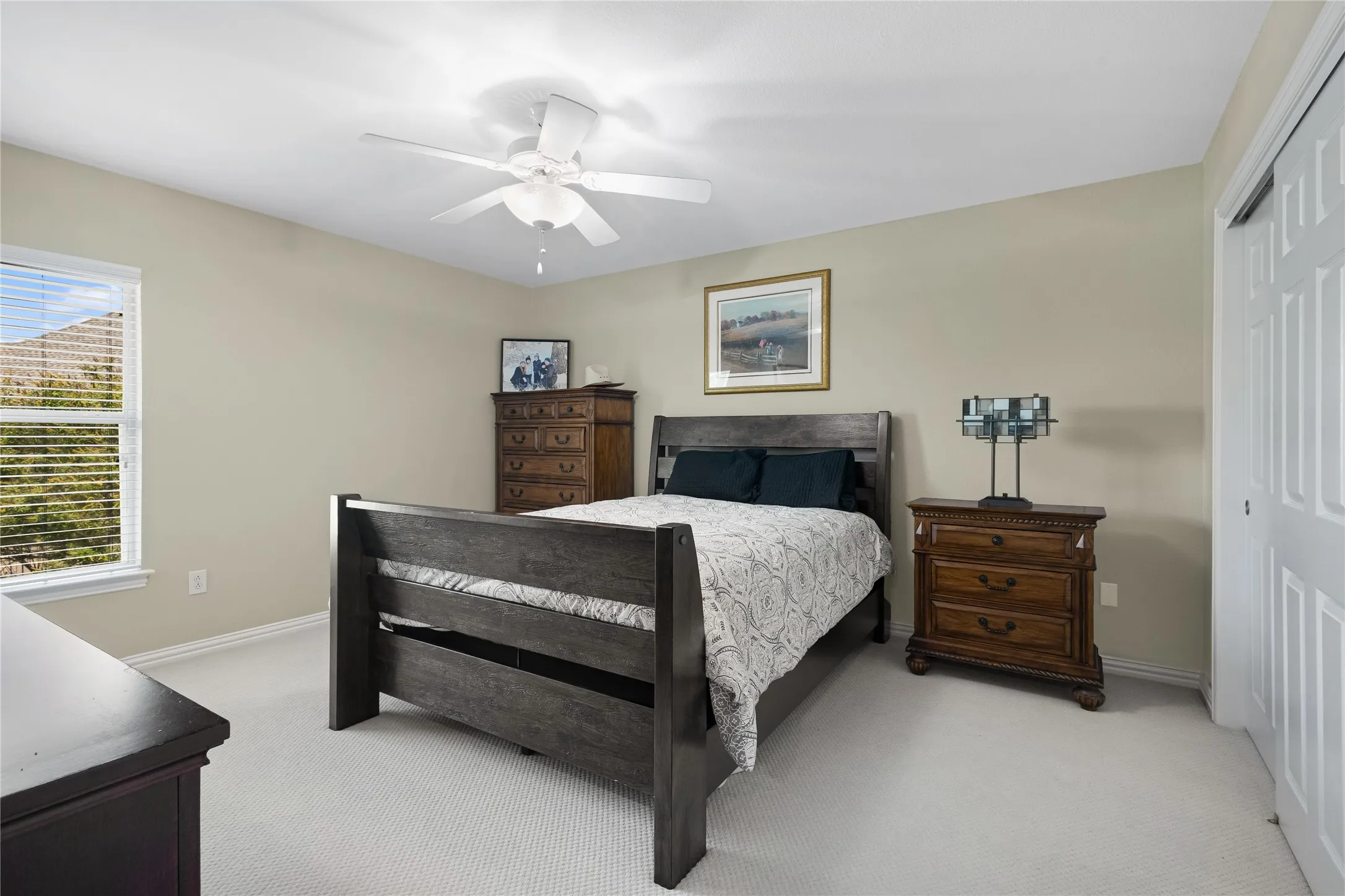 Neutral wall tones, ceiling fan, window with blinds, and light-colored carpeting