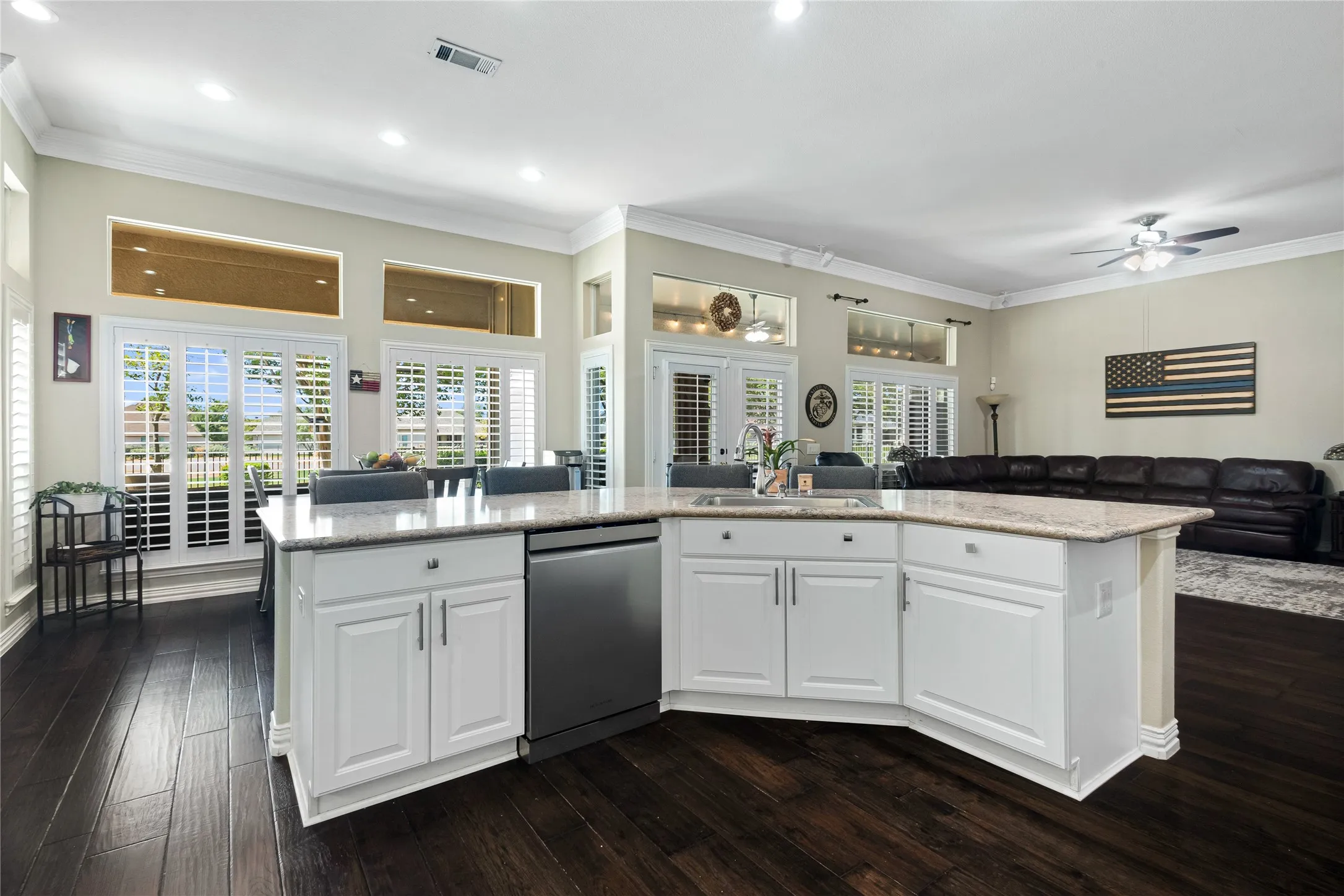 Open-concept kitchen with white cabinetry and a light-toned countertop, integrated stainless steel dishwasher, and dark wood-finish flooring