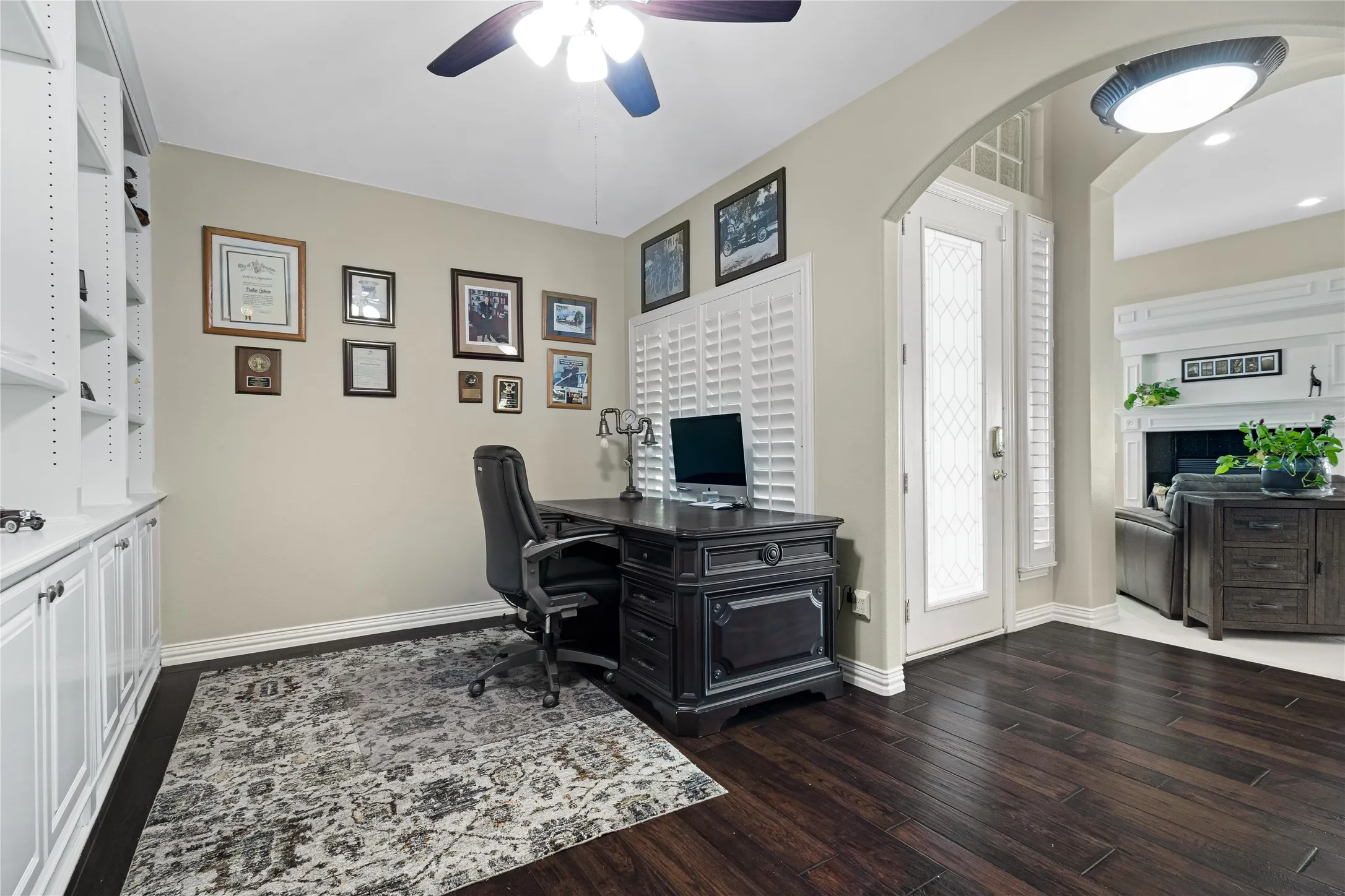 Rich wood-finish flooring, built-in shelving, white plantation shutters, and an arched doorway