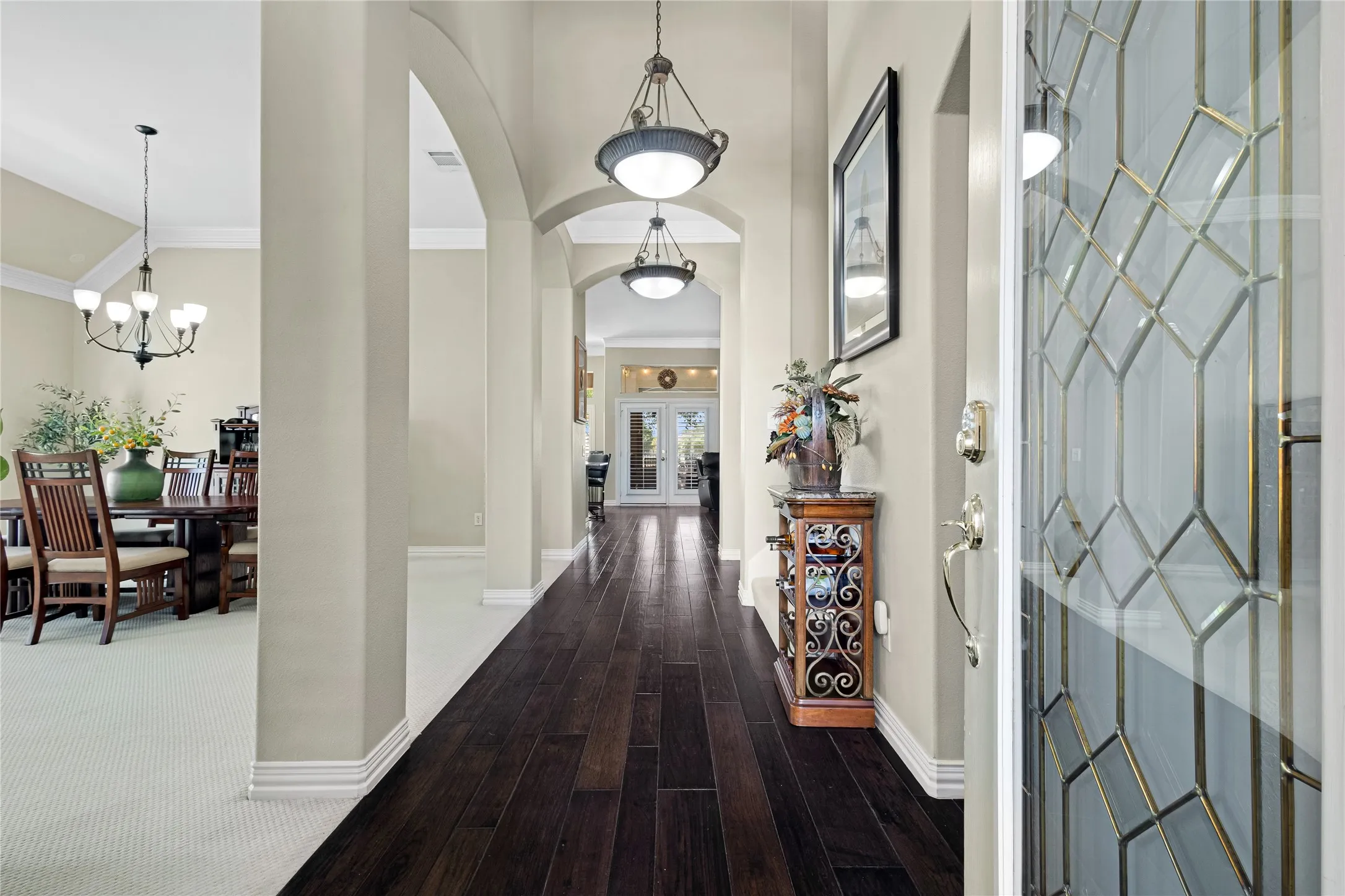 Leaded glass entry door with brass accents, dark wood-finish flooring, arched doorways, and recessed lighting