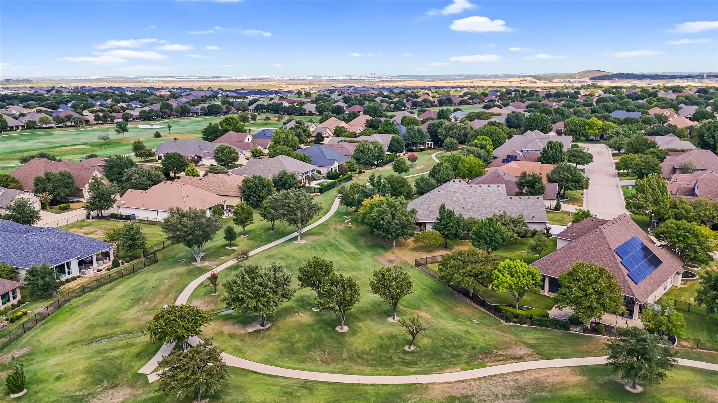 Residential community featuring mature trees, landscaped green space, paved walkways, and golf course access