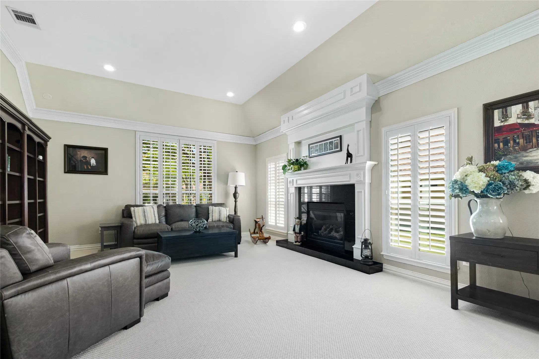 Vaulted ceiling, recessed lighting, white crown molding, plantation shutters, and a fireplace with a black surround and white mantel
