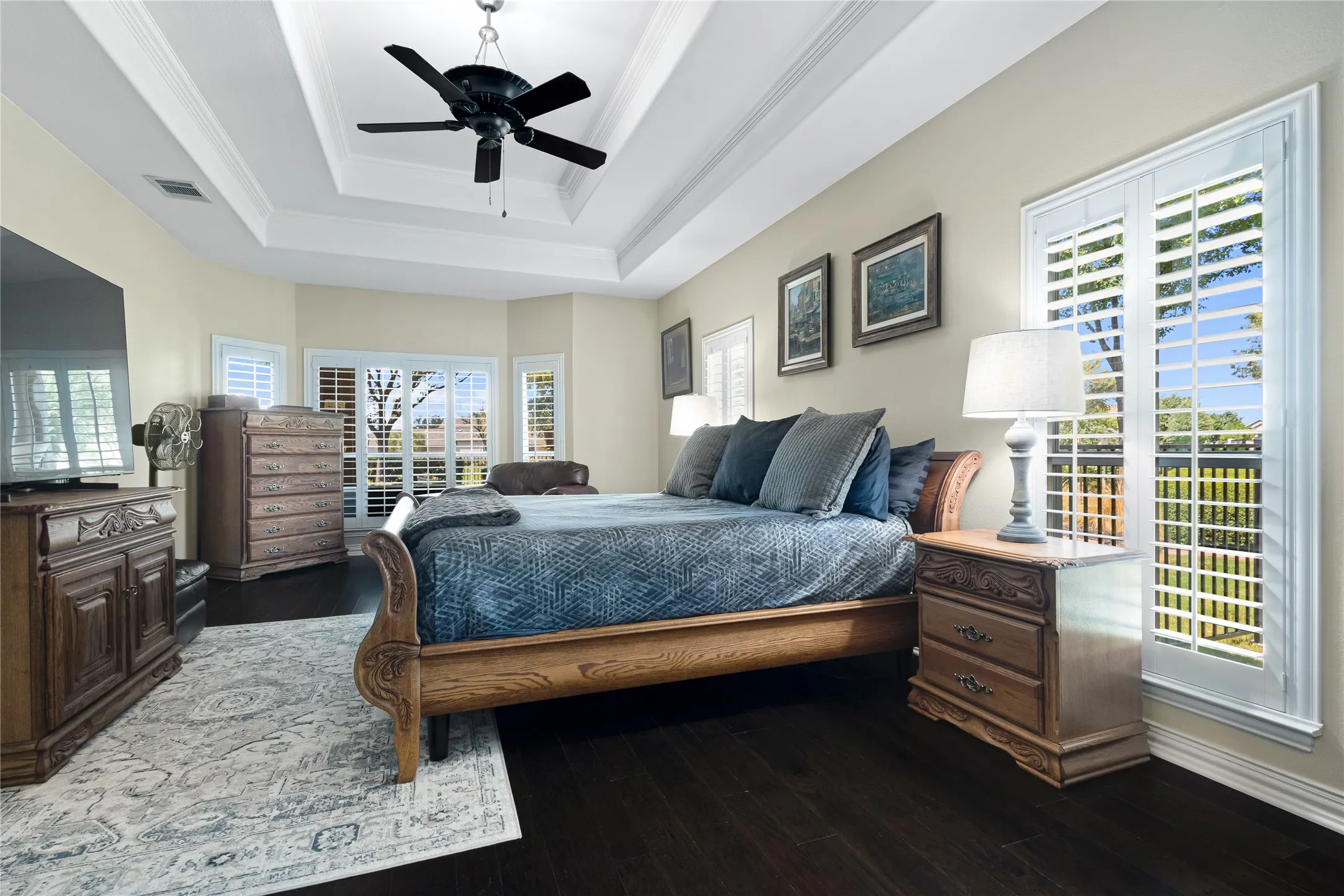 Tray ceiling with a ceiling fan, dark wood-finish flooring, multiple windows with plantation shutters, and light-toned wall paint