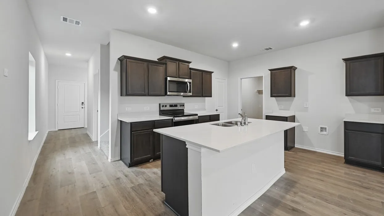 Modern kitchen featuring dark wood cabinetry, stainless steel appliances, a center island with an undermount double-basin sink, and light-toned countertops