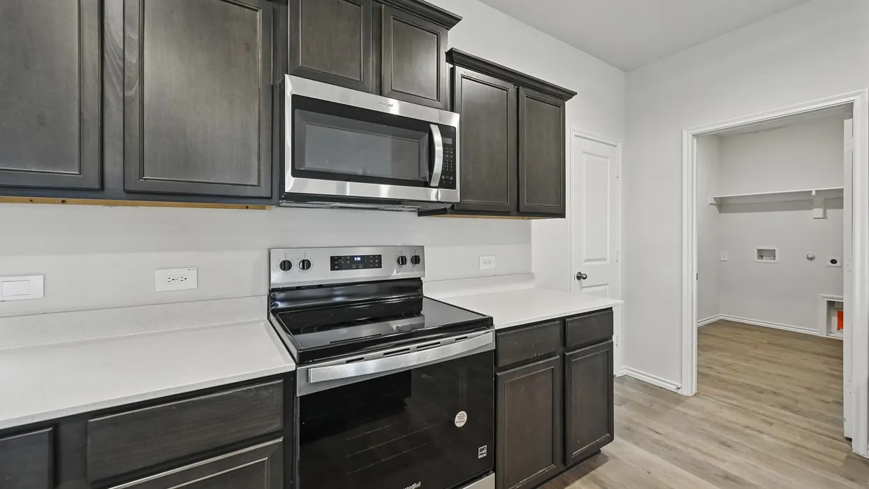 Kitchen featuring dark wood-finish cabinetry, stainless steel appliances including an over-range microwave and electric range, and light-colored countertops