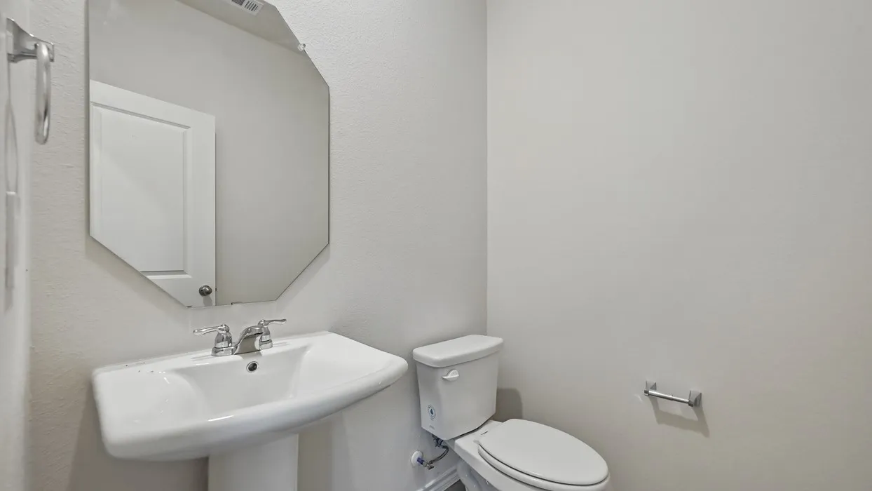 Pedestal sink with chrome faucet, complemented by an octagonal mirror