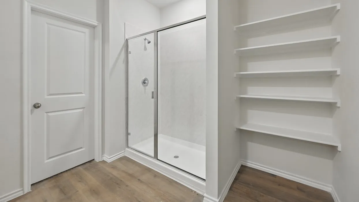 Glass-enclosed shower with a white base, surrounded by wood-finish flooring and multiple built-in shelving units