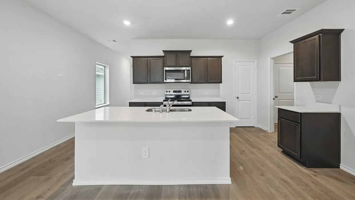 Kitchen featuring a large island with an undermount sink, dark wood-finish cabinetry, light countertops, wood-finish flooring, and recessed lighting