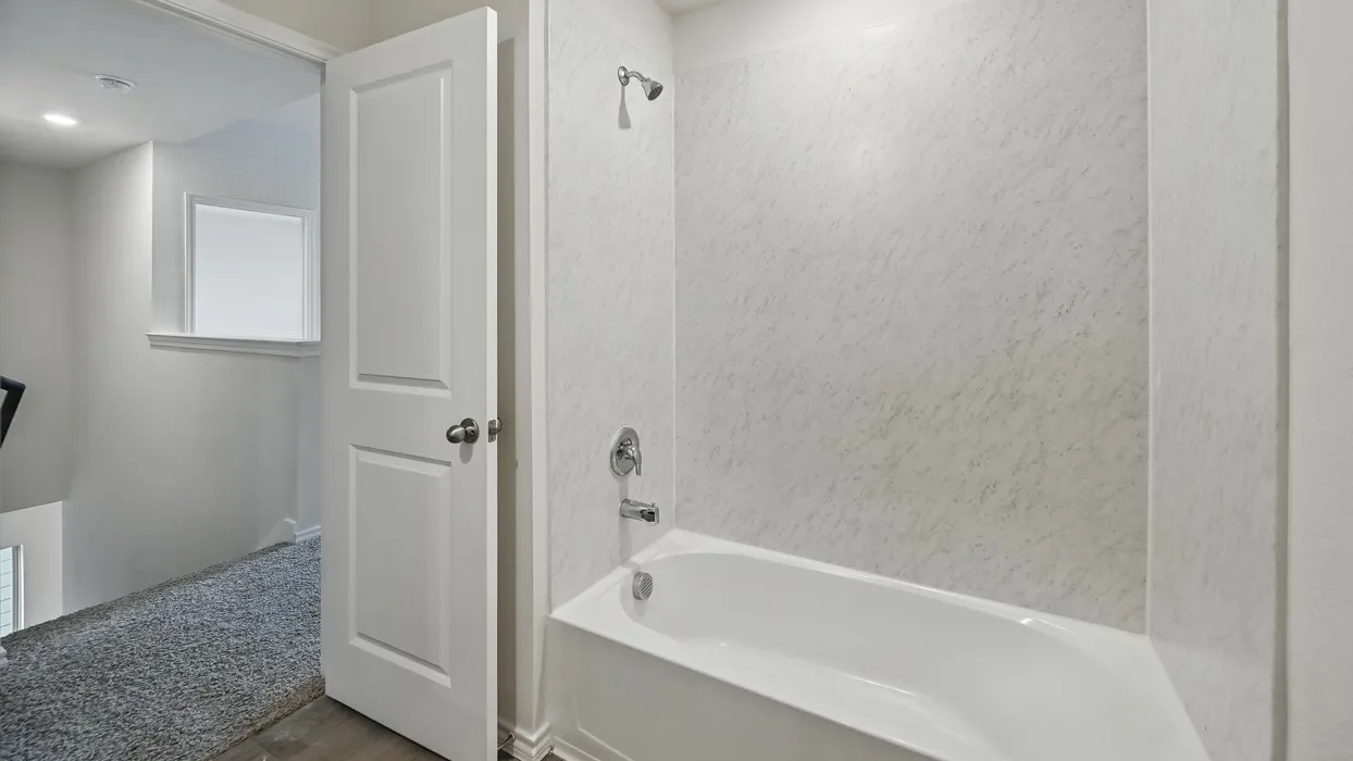 Bathtub with shower fixture and textured wall surround