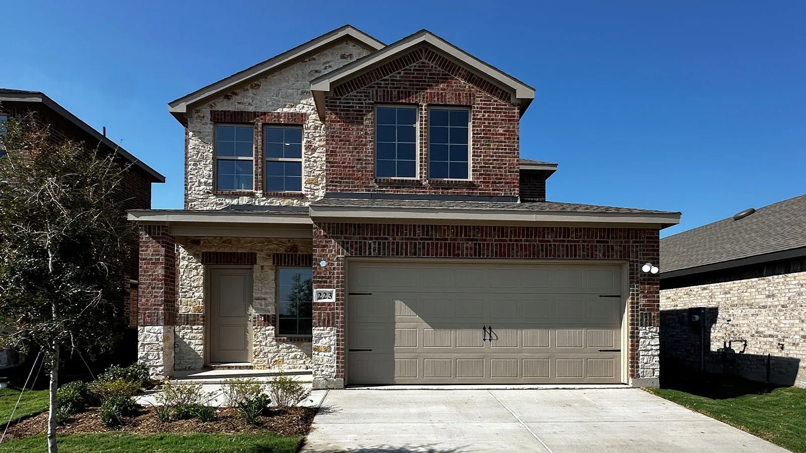 Two-story residence featuring a brick and stone facade, covered porch entry, and an attached two-car garage