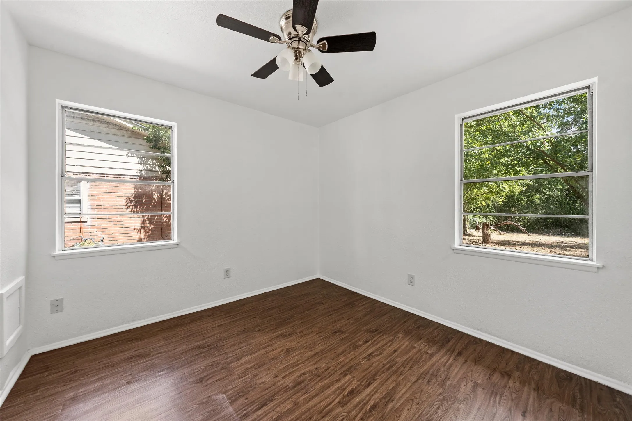 White painted walls, wood-finish flooring, two windows, and a ceiling fan with light fixture