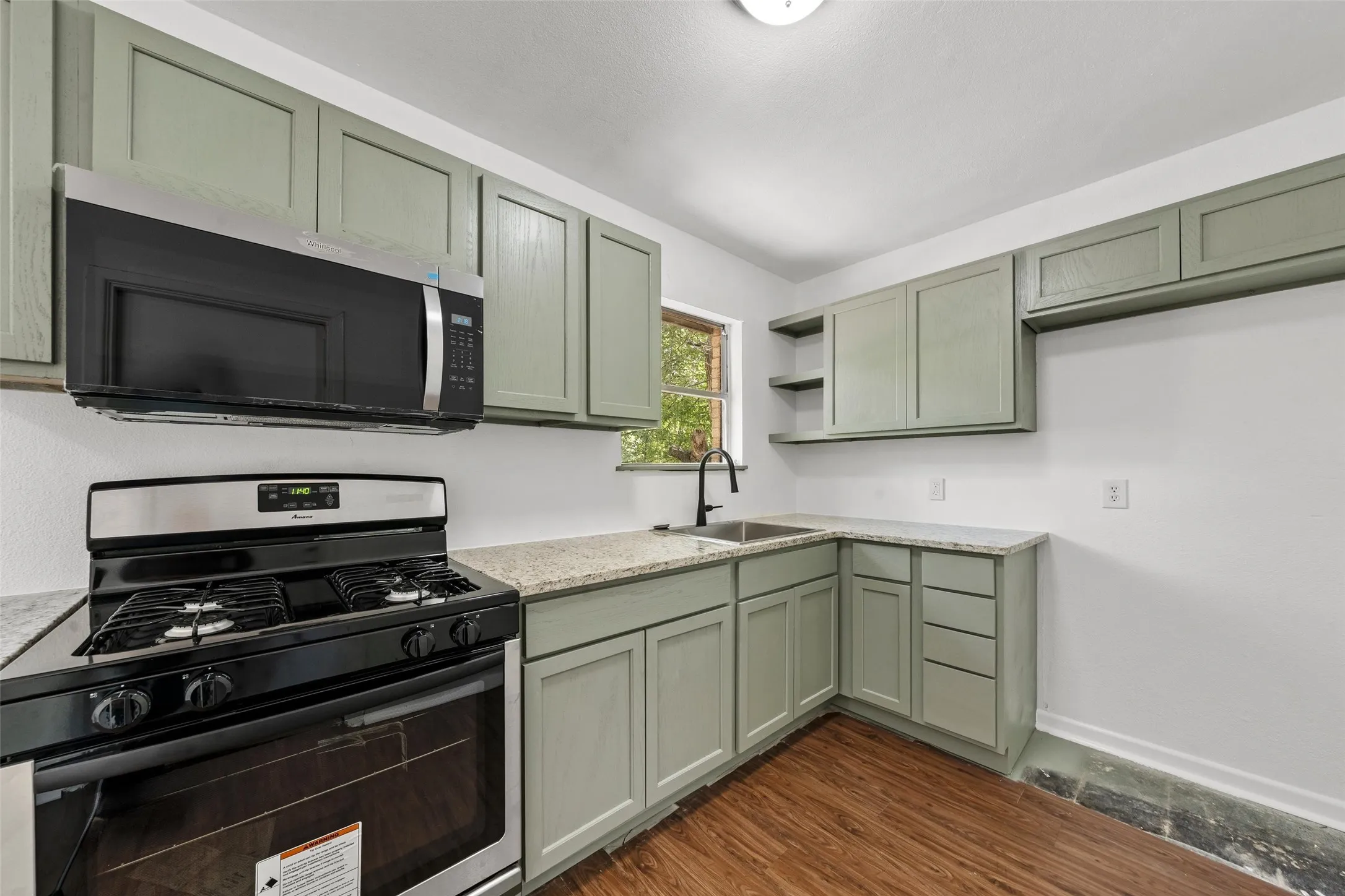 Stainless steel microwave, gas range, wood-finish flooring, light-toned cabinetry, and light-toned countertops