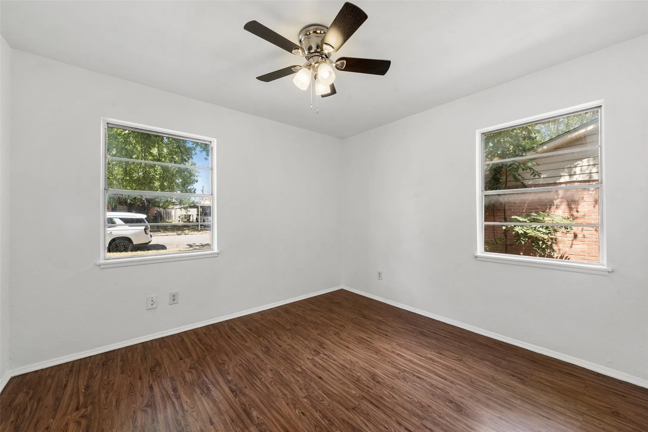 Wood-finish flooring throughout, white painted walls, and a ceiling fan with integrated lighting