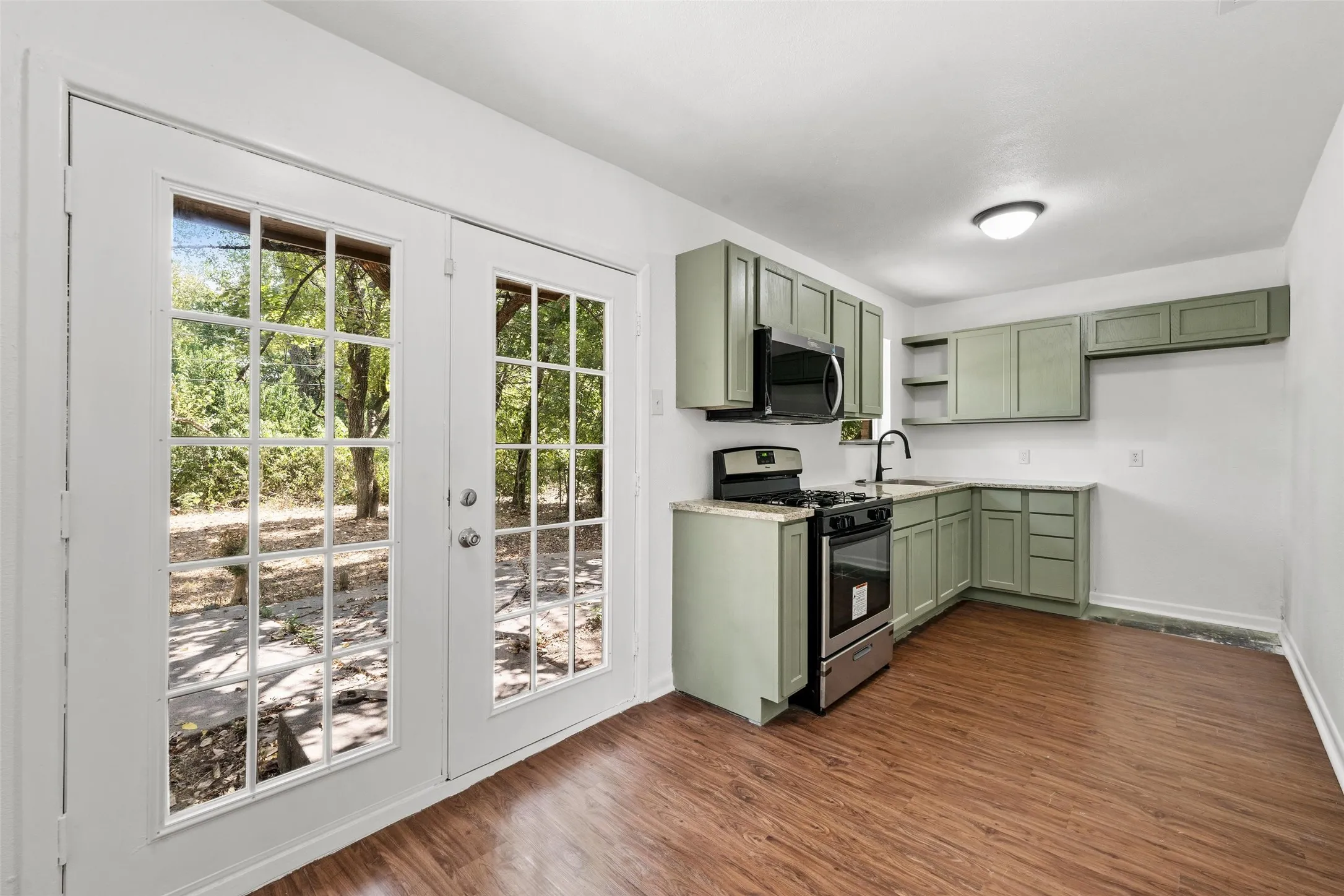 Kitchen with light green cabinetry, stainless steel appliances, wood-finish flooring, and white walls