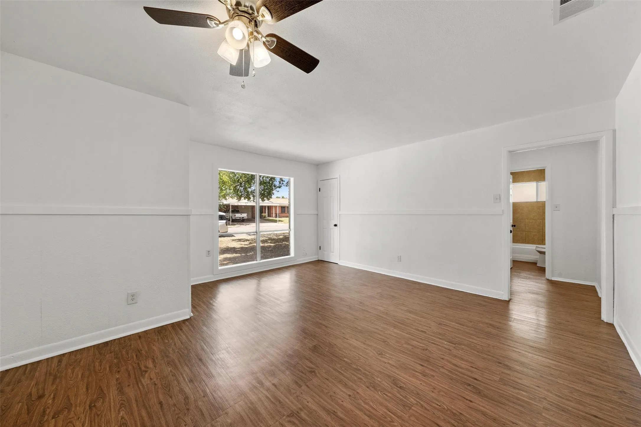Wood-finish flooring throughout, white painted walls, and a ceiling fan with integrated lighting