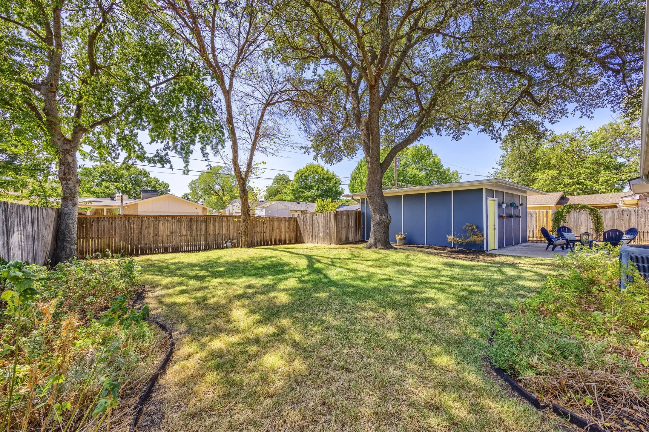 Spacious backyard featuring a manicured lawn, established shade trees, and a privacy fence