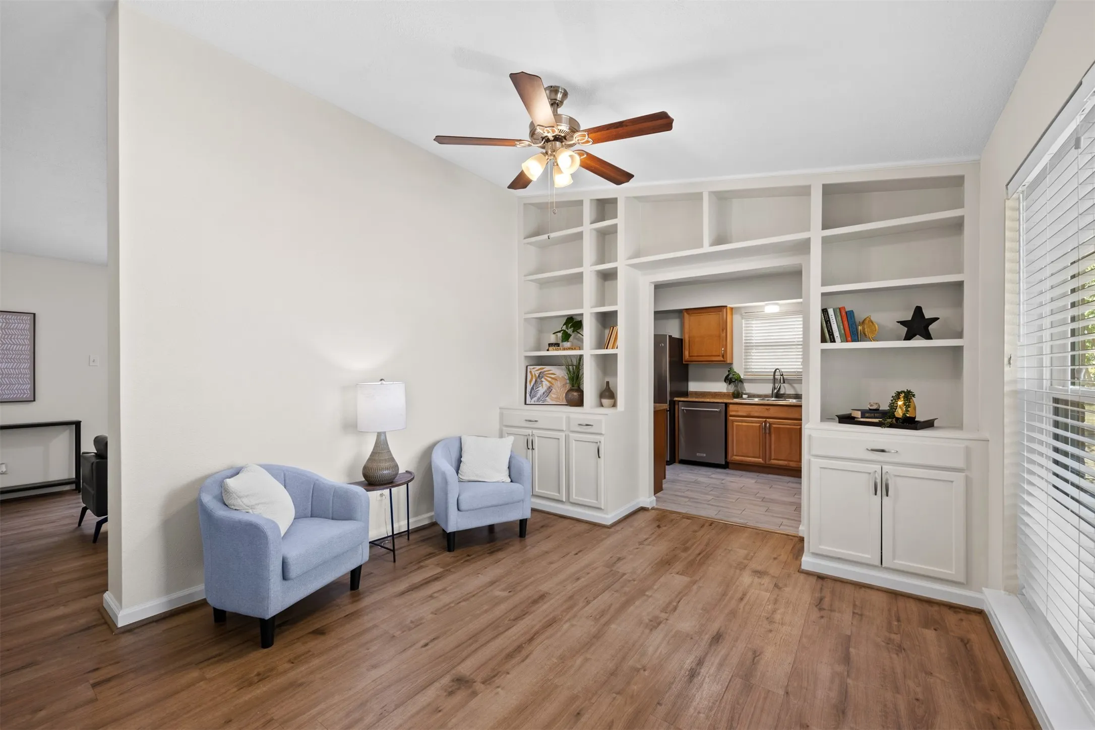 Wood-finish flooring, built-in shelving, ceiling fan with light fixture, and window with blinds