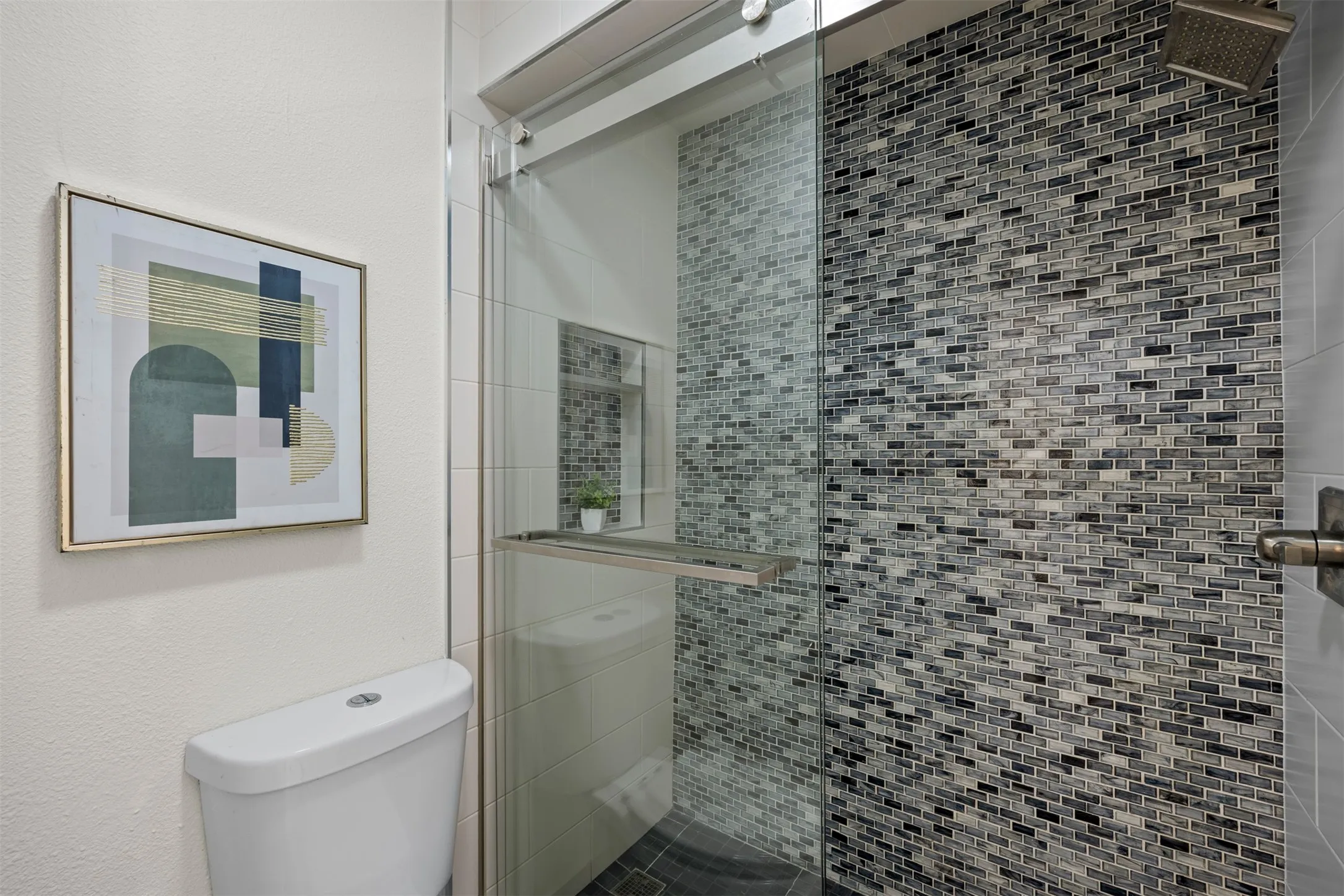 Glass-enclosed shower with mosaic tile surround, rainfall showerhead, and a fixed toilet
