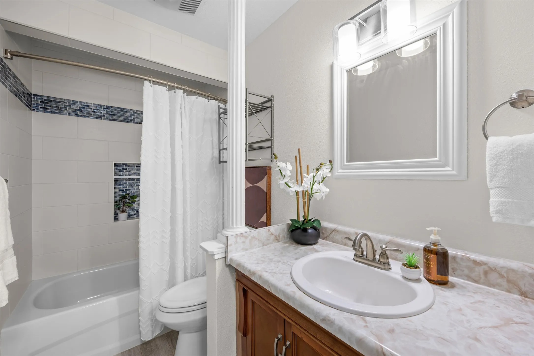 Vanity with an integrated sink and light-toned countertop, wood-finish cabinetry, and a framed mirror with an overhead vanity light