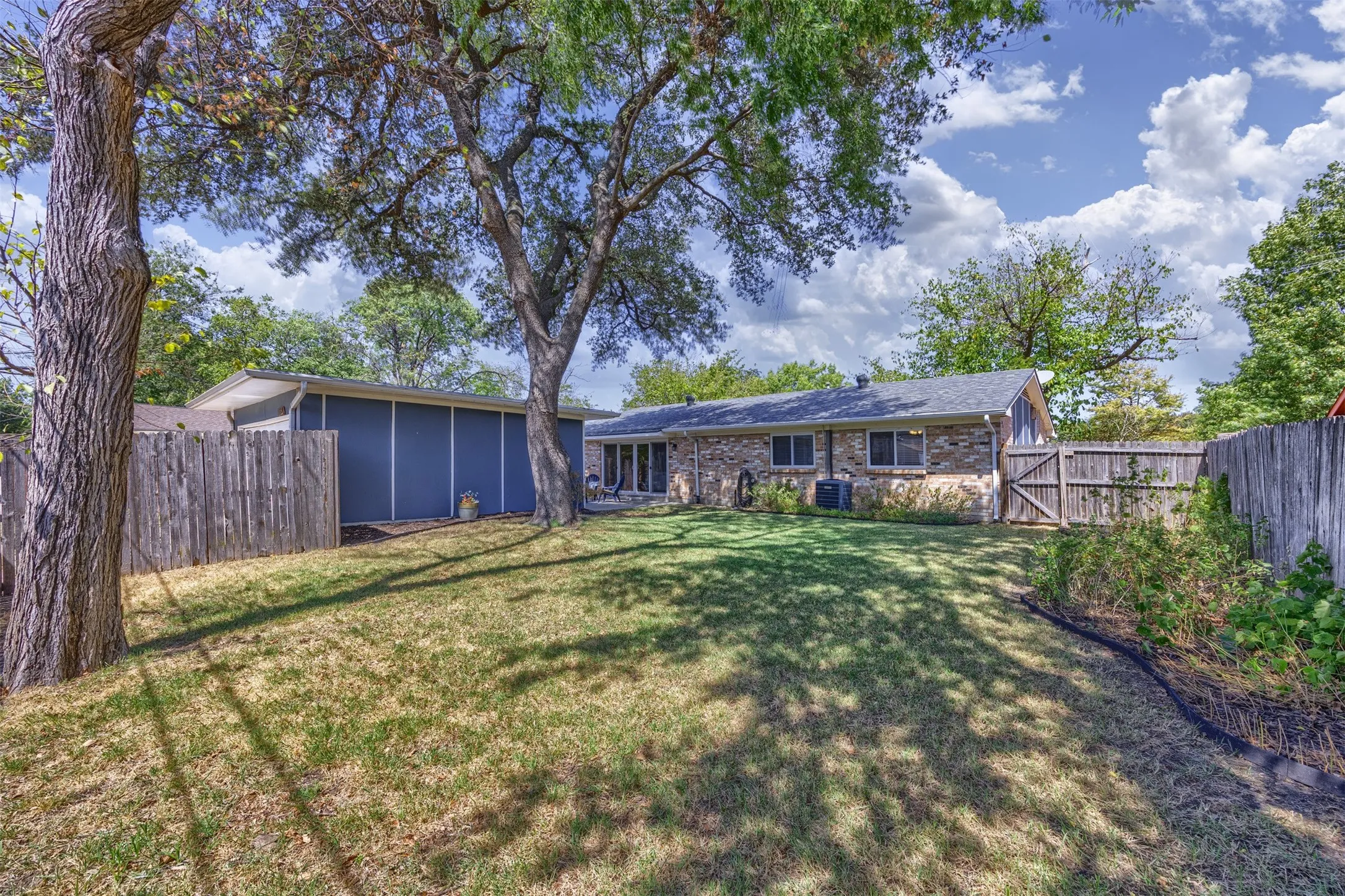 Expansive backyard featuring a manicured lawn, mature shade trees, and a wooden privacy fence