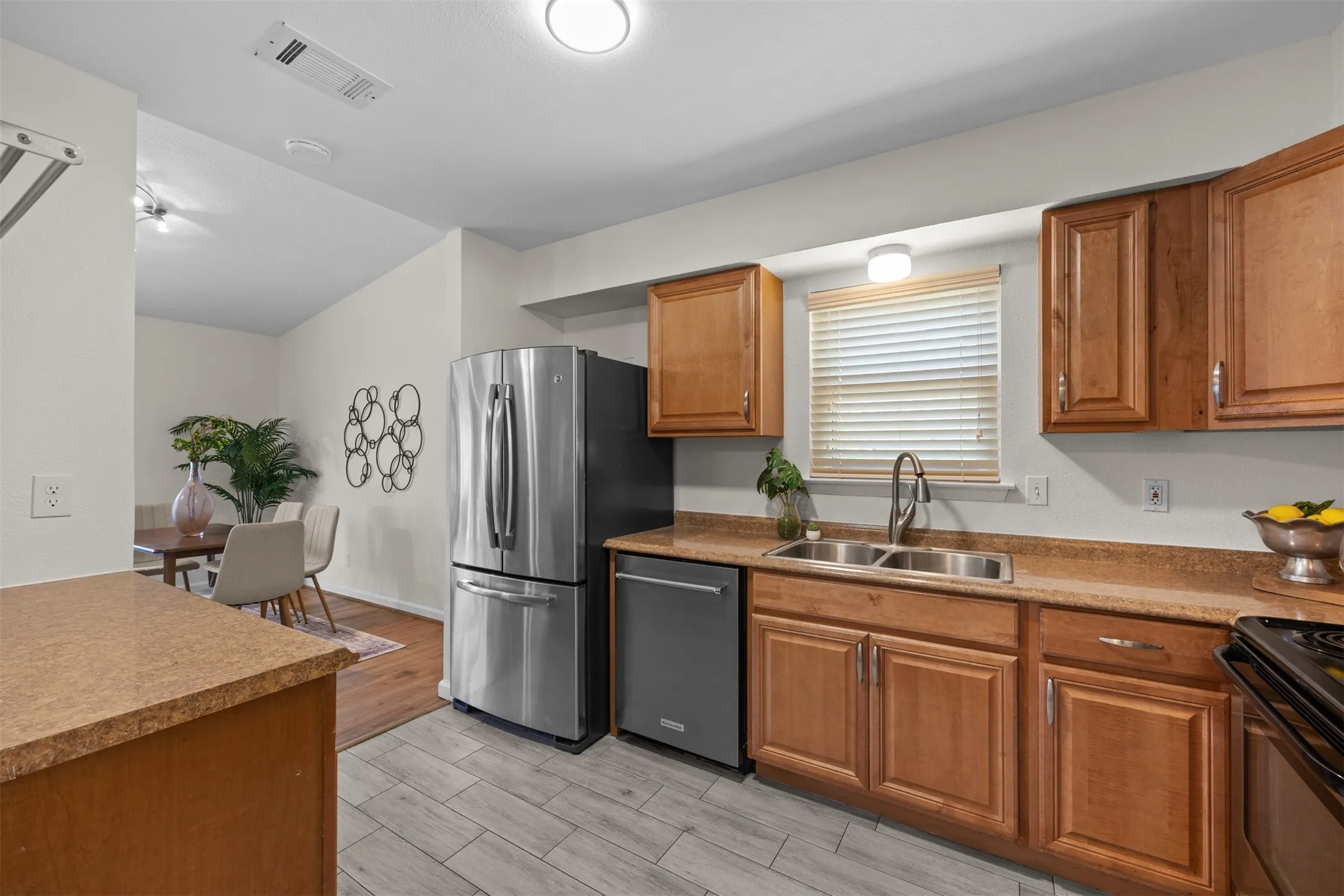 Updated kitchen featuring wood cabinetry, stone-look countertops, stainless steel appliances, and a double basin sink