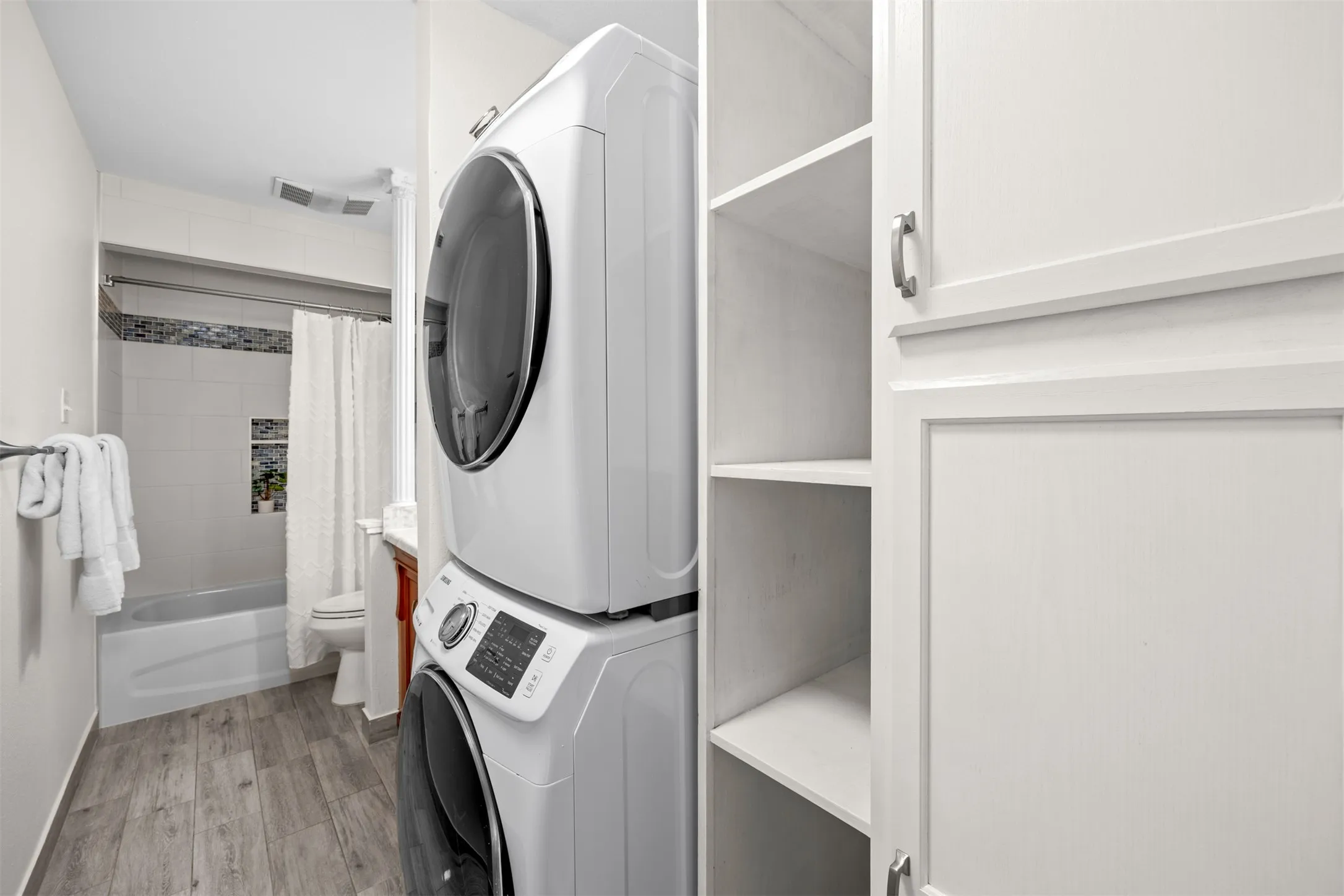 Dedicated laundry area with stacked appliances, white shaker-style cabinetry, and open shelving