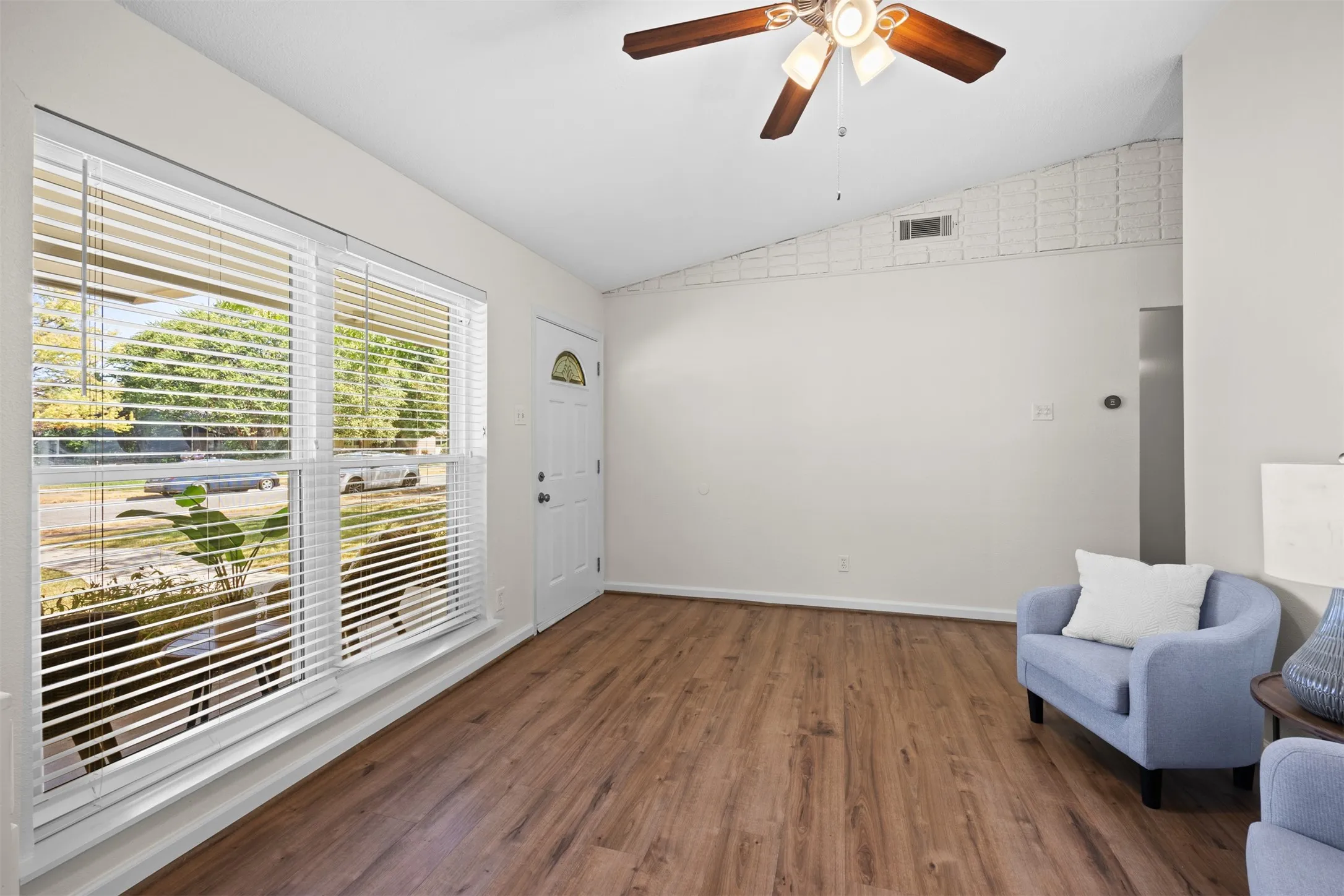 Vaulted ceiling with a ceiling fan, wood-finish flooring, and a window with blinds