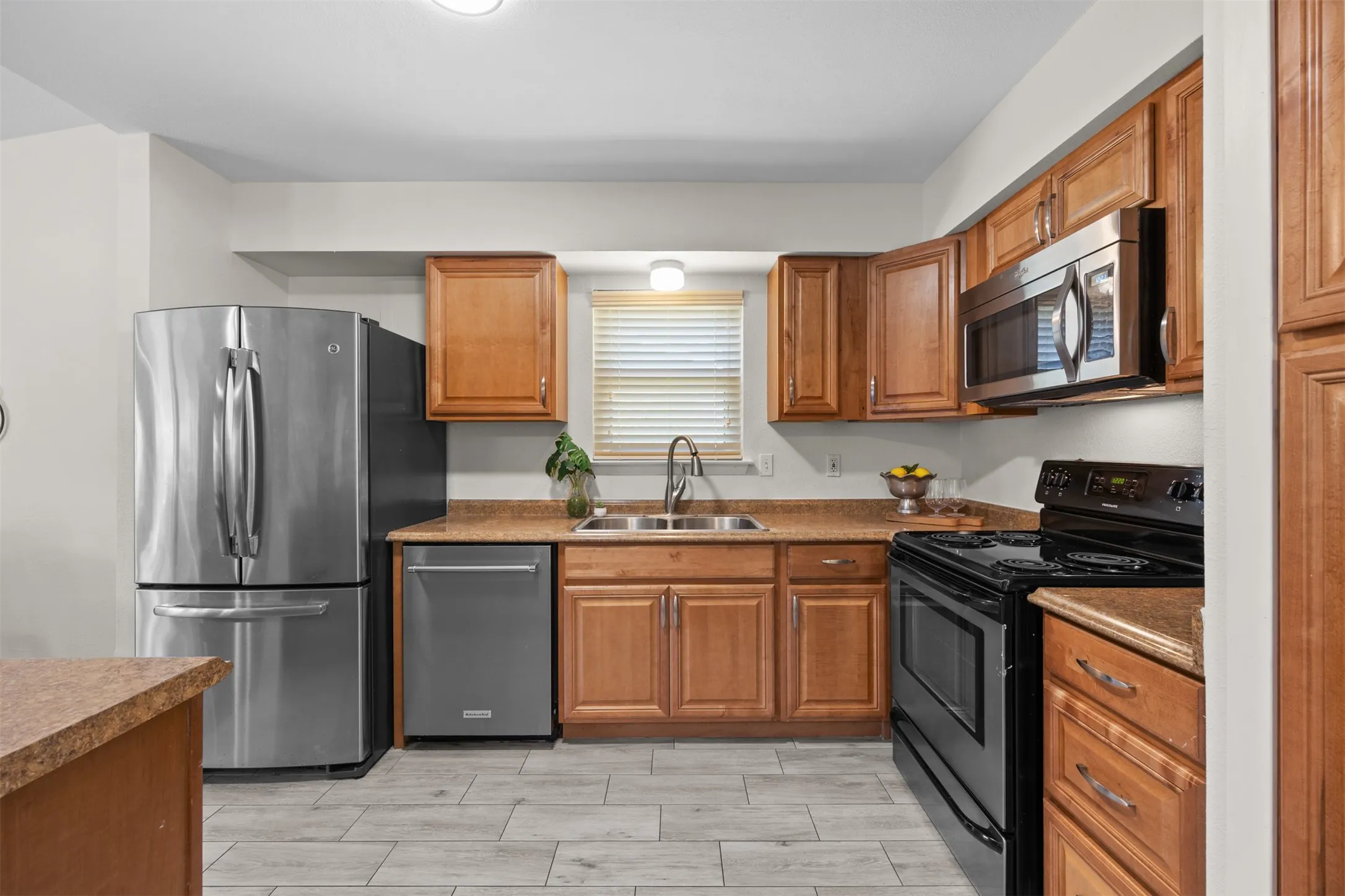 Kitchen featuring wood cabinetry, stainless steel appliances, a black range, a double basin sink, and wood-finish flooring