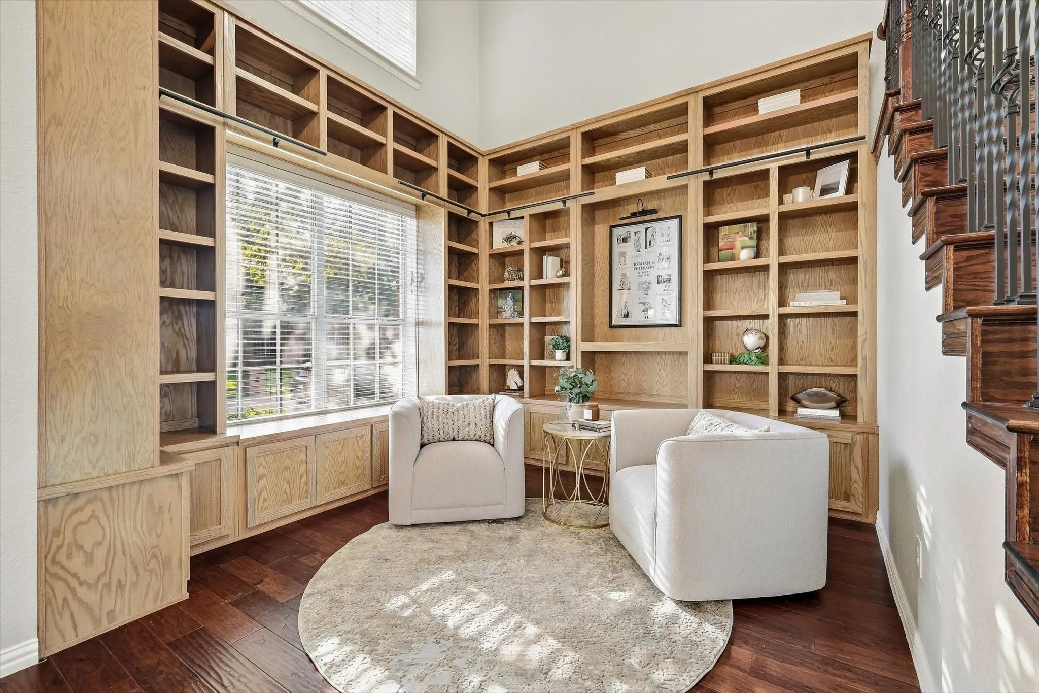 Hardwood flooring, natural wood built-in shelving, built-in window seating, and a grand staircase with dark wood treads and wrought iron balusters