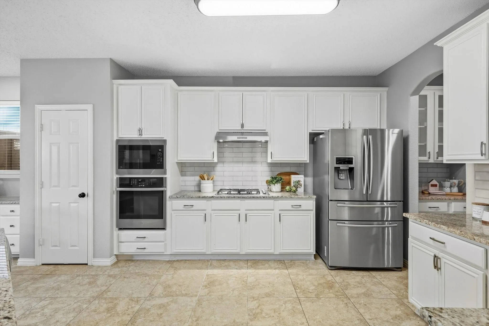 Kitchen featuring white cabinetry, stainless steel appliances, a subway tile backsplash, granite countertops, and tile flooring