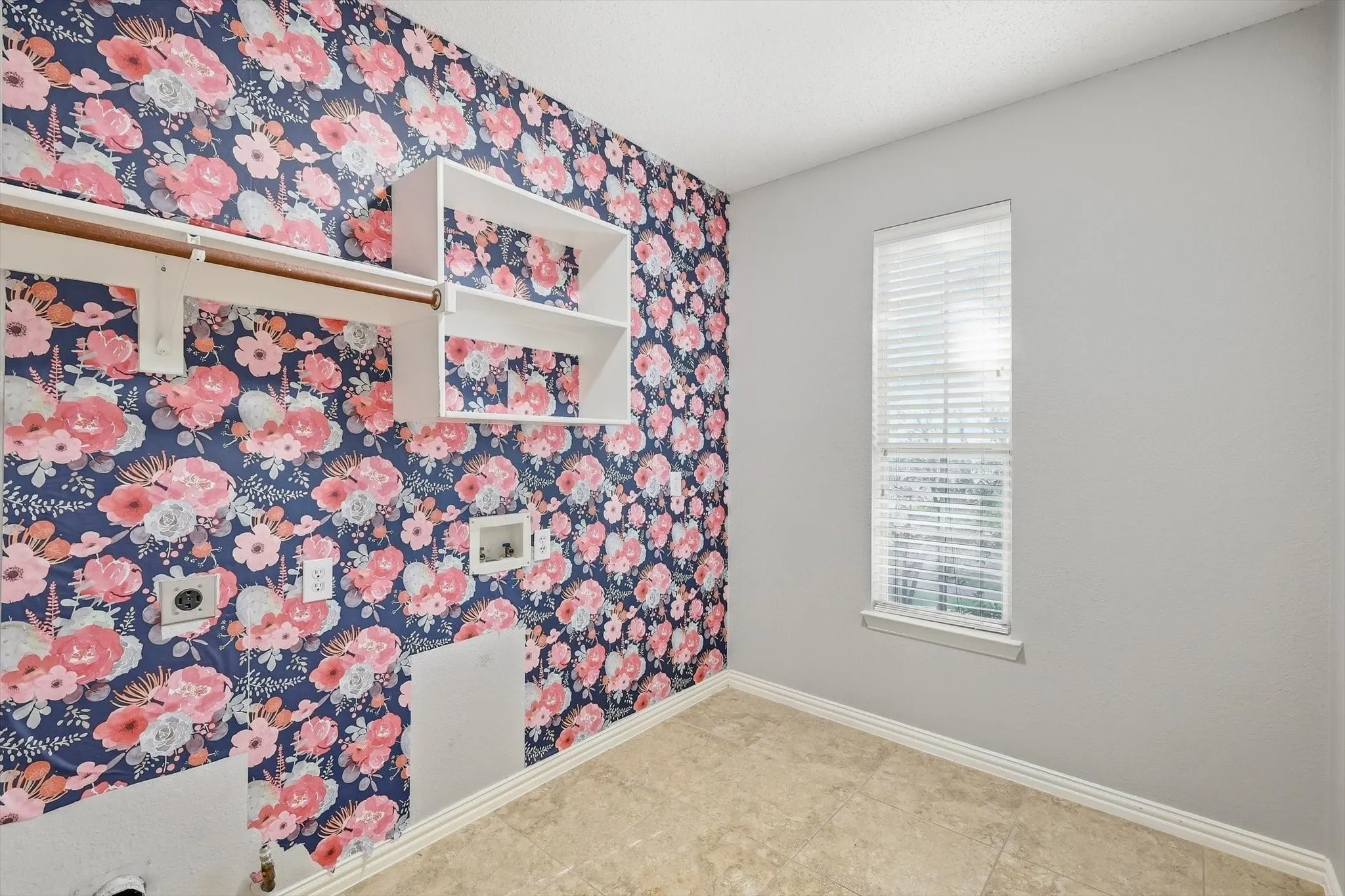 Built-in shelving, built-in clothing rod, window with blinds, tile flooring, and a patterned accent wall