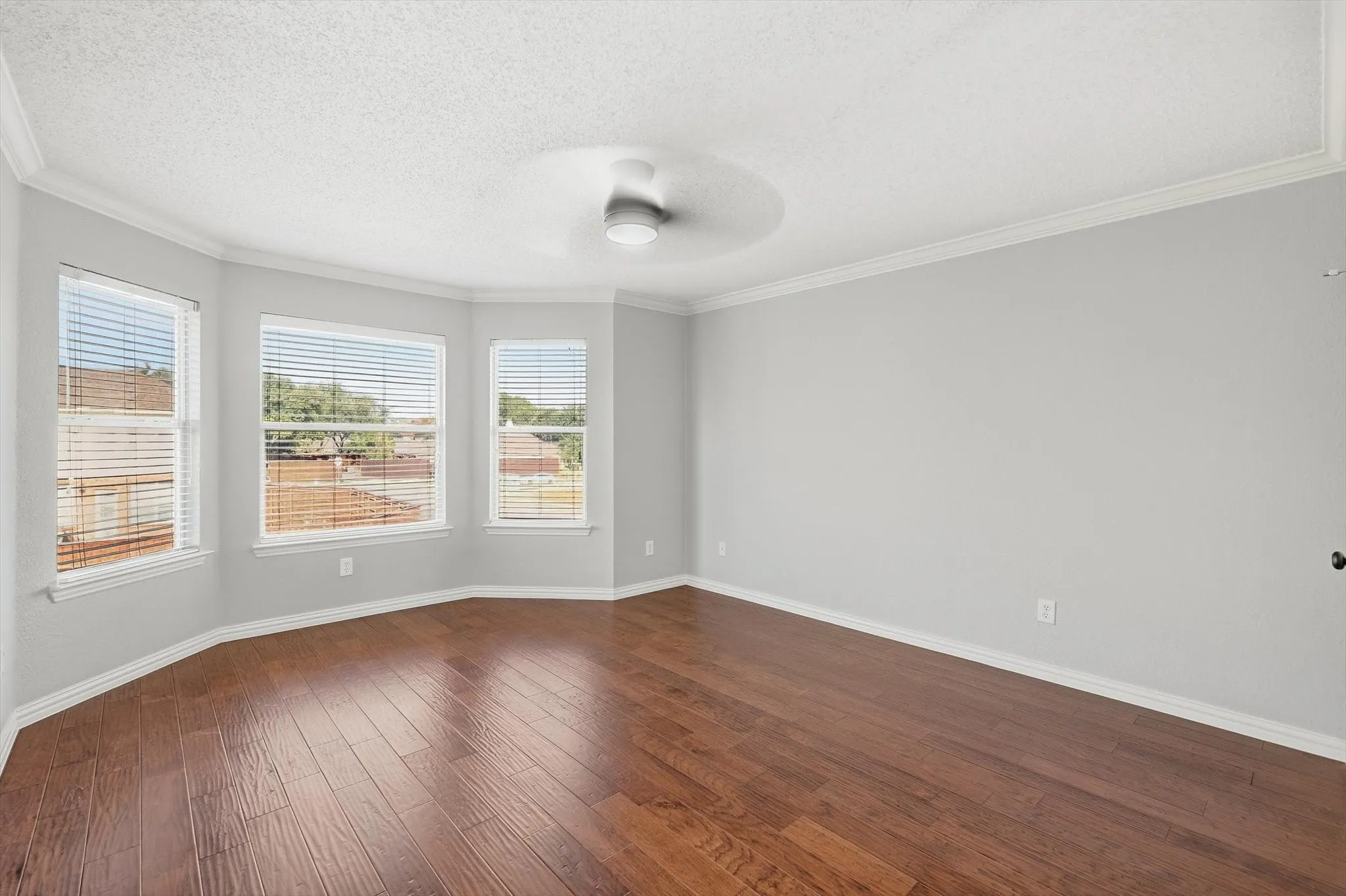 Wood-finish flooring, multiple windows, crown molding, and a ceiling fan