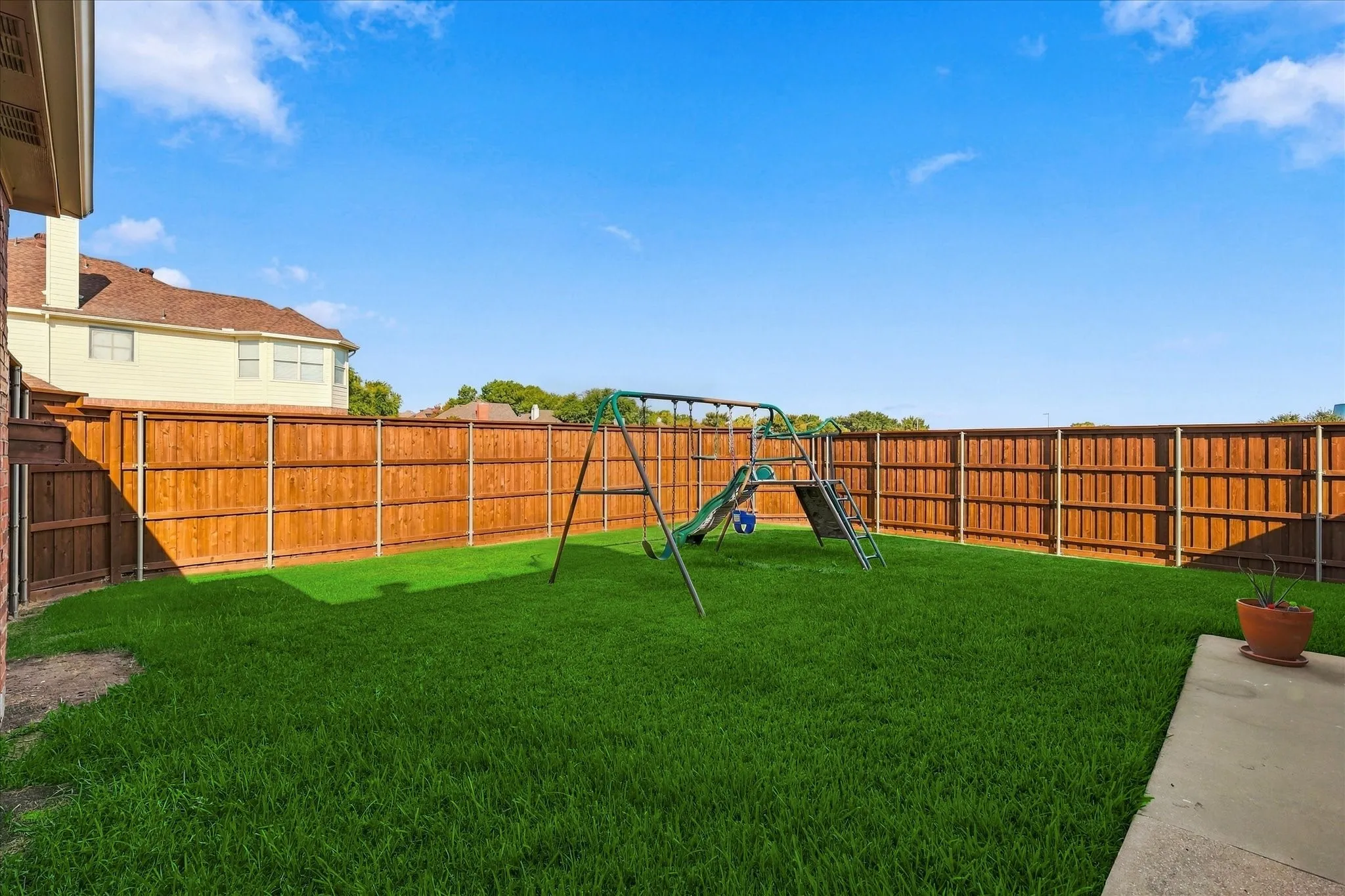 Expansive fenced backyard featuring a manicured lawn and a concrete patio area
