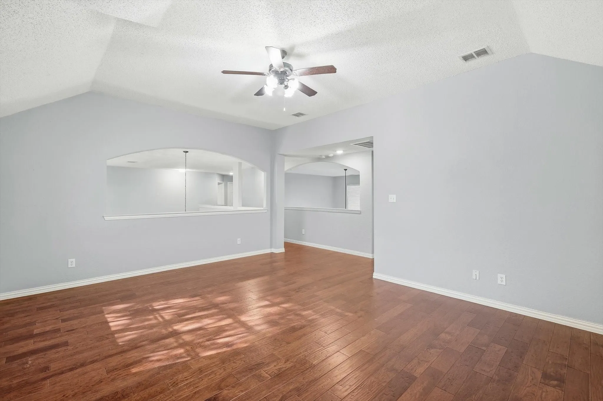 Vaulted ceilings with a ceiling fan, wood-finish flooring, and arched wall cutouts
