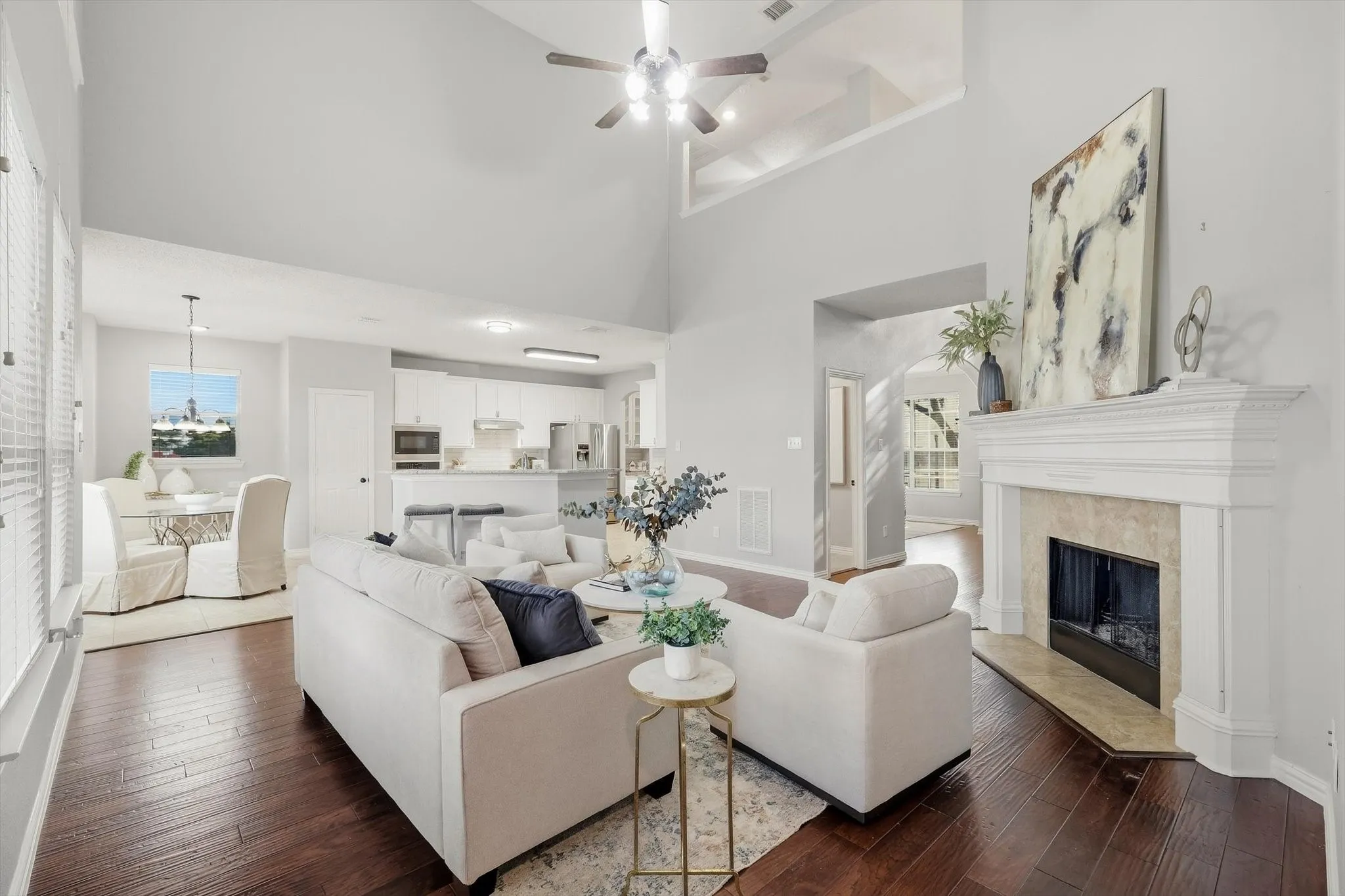 Vaulted ceiling living area with a ceiling fan, fireplace featuring a carved wood mantel and stone surround, and wood-finish flooring