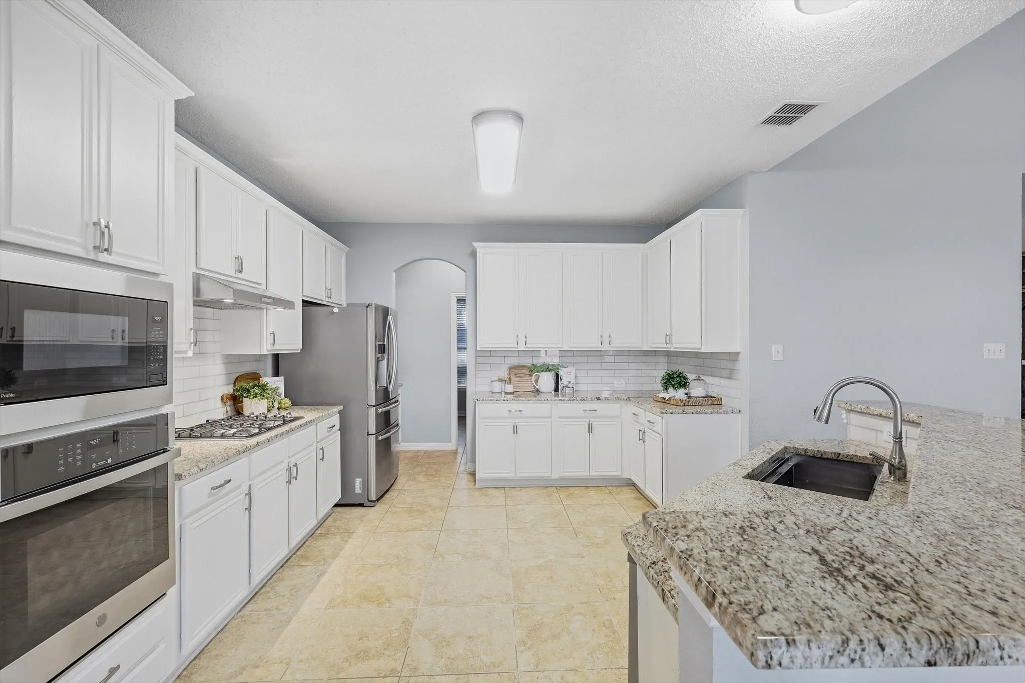 Kitchen featuring white cabinetry, light-toned countertops, stainless steel appliances, a tiled backsplash, and neutral-toned flooring