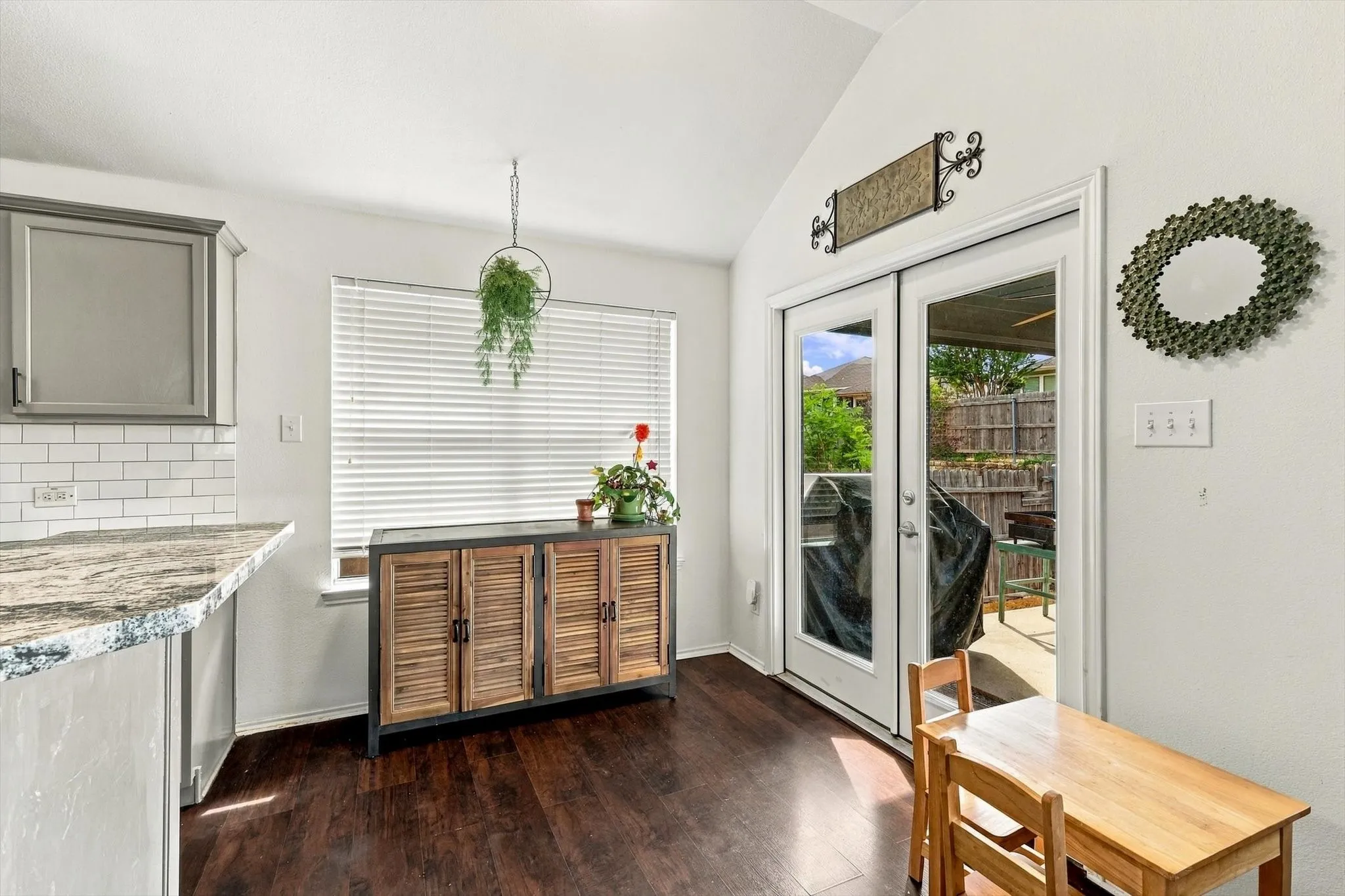 Vaulted ceiling, wood-finish flooring, white subway tile backsplash, light-toned cabinetry, and double glass-paneled doors
