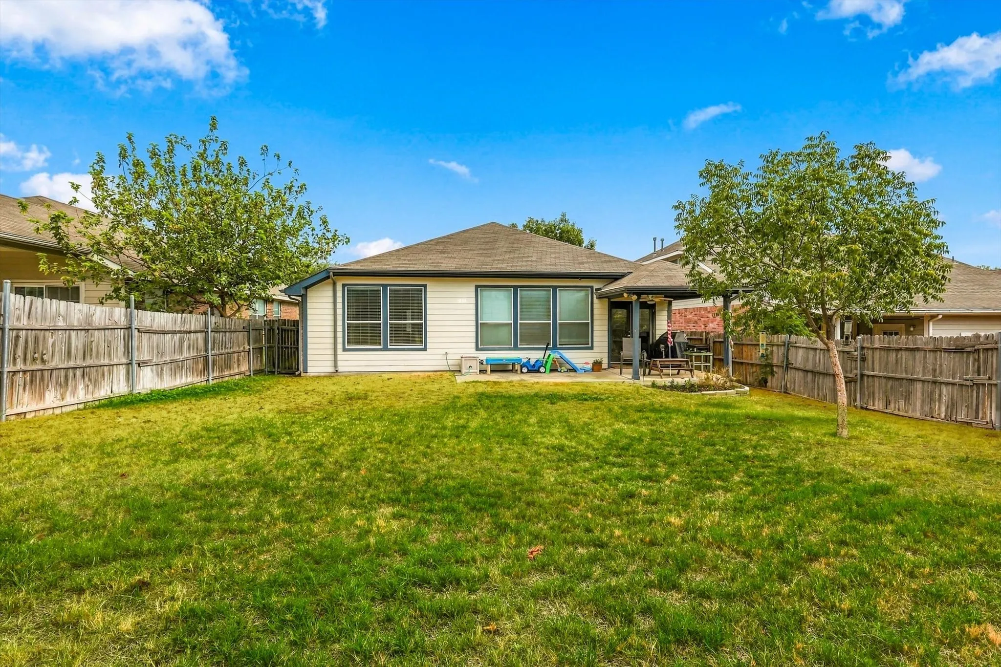 Expansive backyard featuring a lush lawn, privacy fencing, and a covered patio