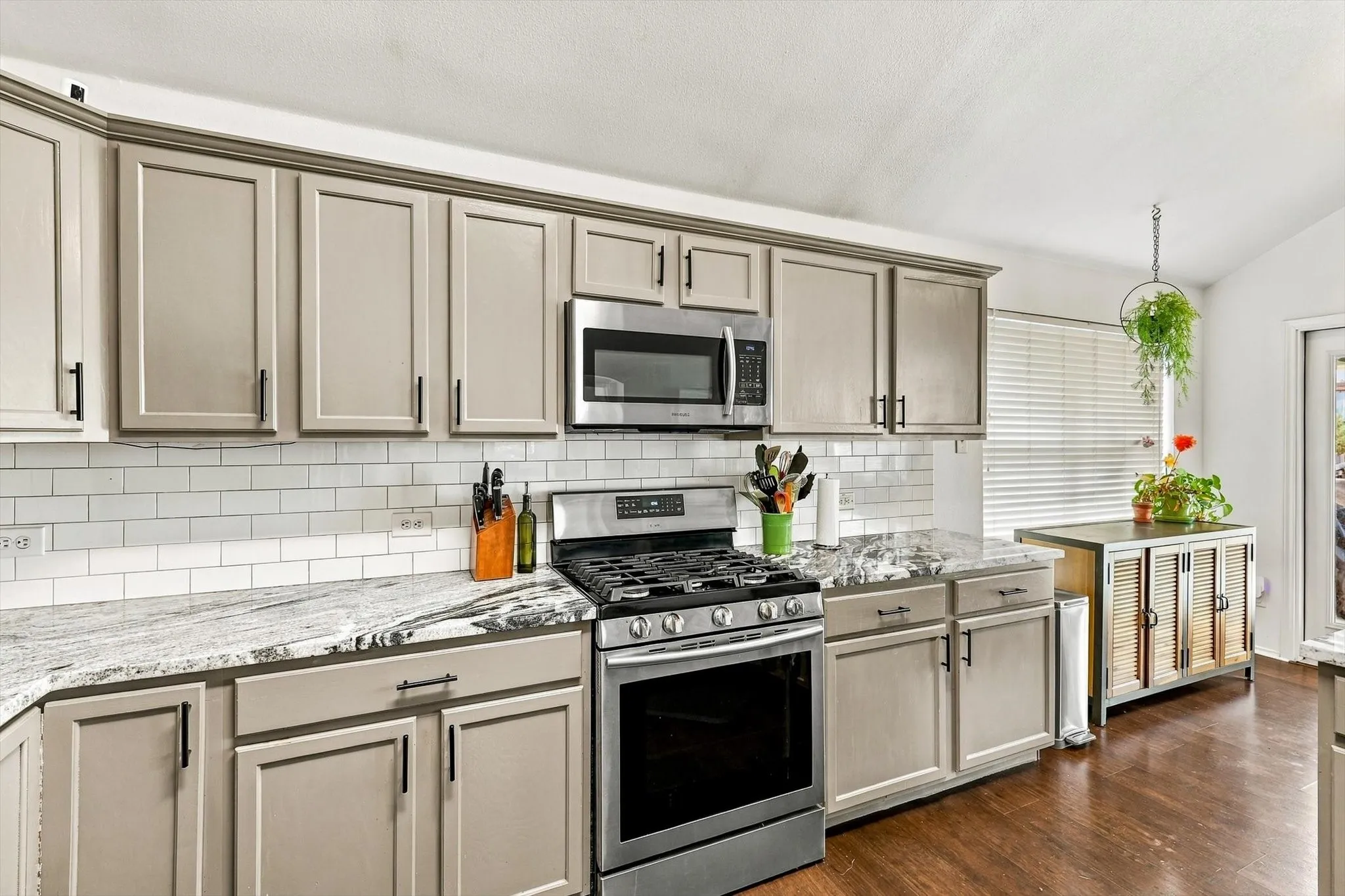 Kitchen featuring light-toned cabinetry with dark hardware, stainless steel range, built-in microwave, white subway tile backsplash, and patterned countertops