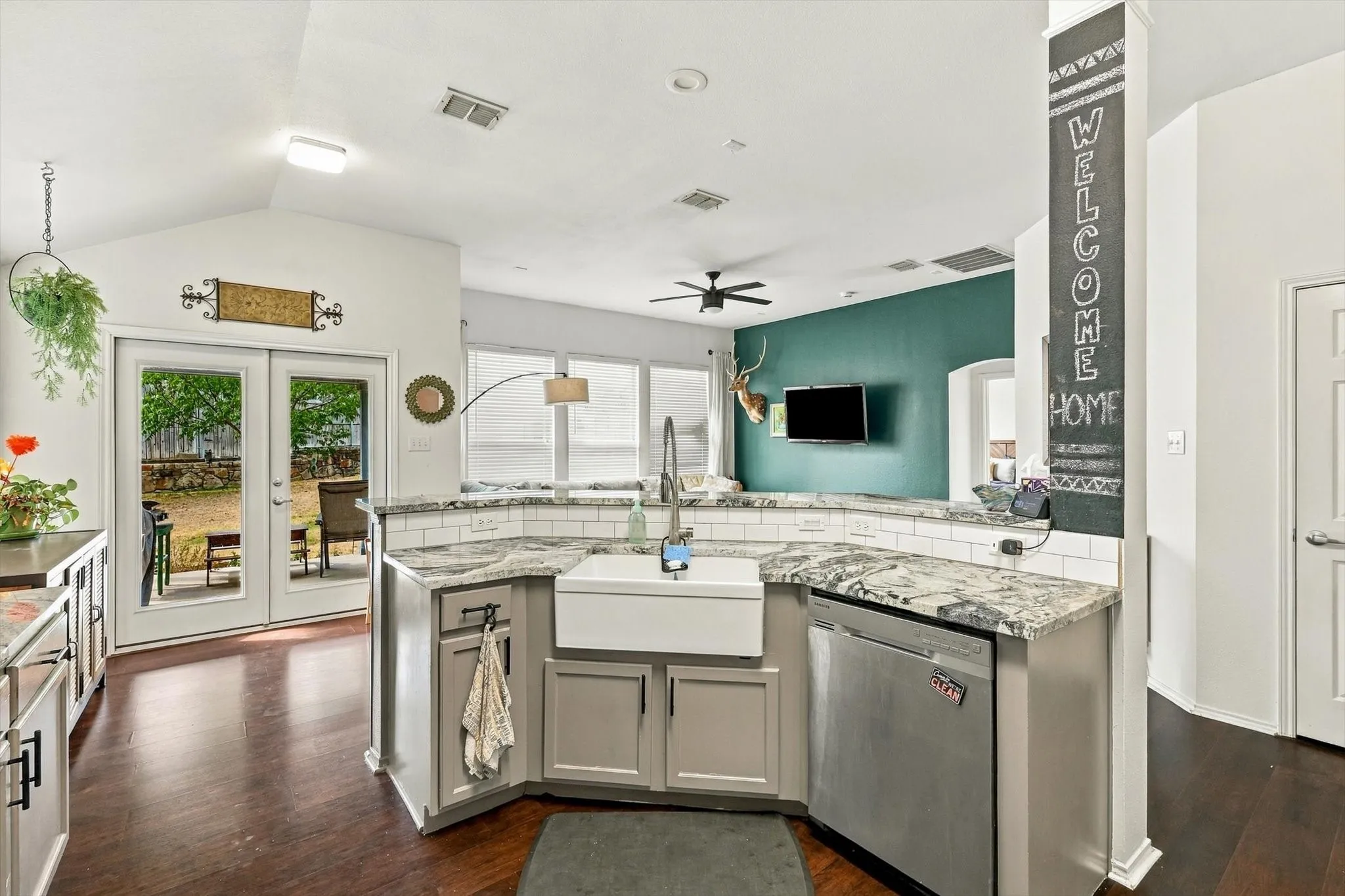 Kitchen featuring a white farmhouse sink, stainless steel dishwasher, white subway tile backsplash, and light-colored cabinetry with dark hardware