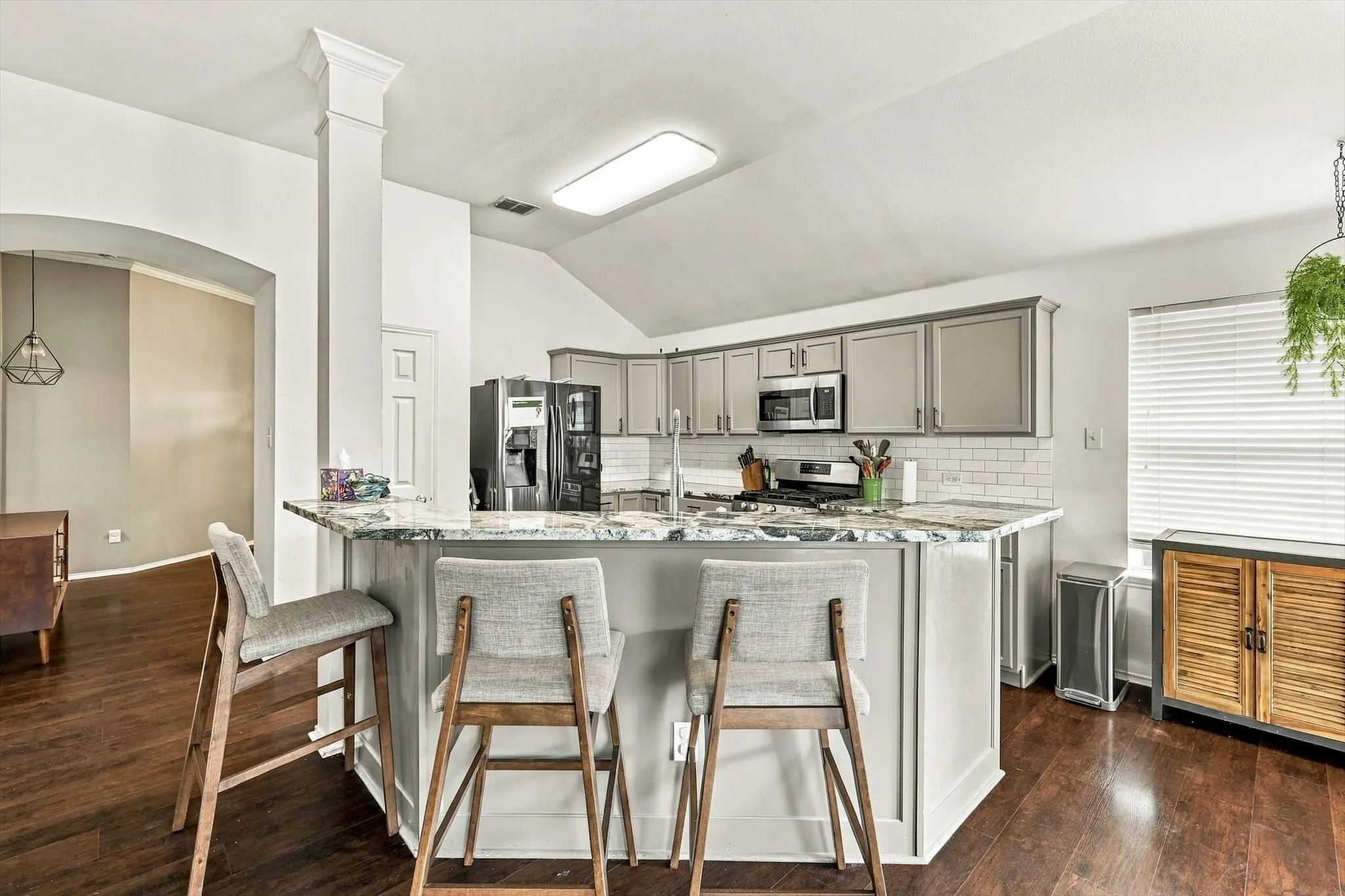 Kitchen featuring wood-finish flooring, a kitchen island with stone-finish countertop, subway tile backsplash, and stainless steel appliances
