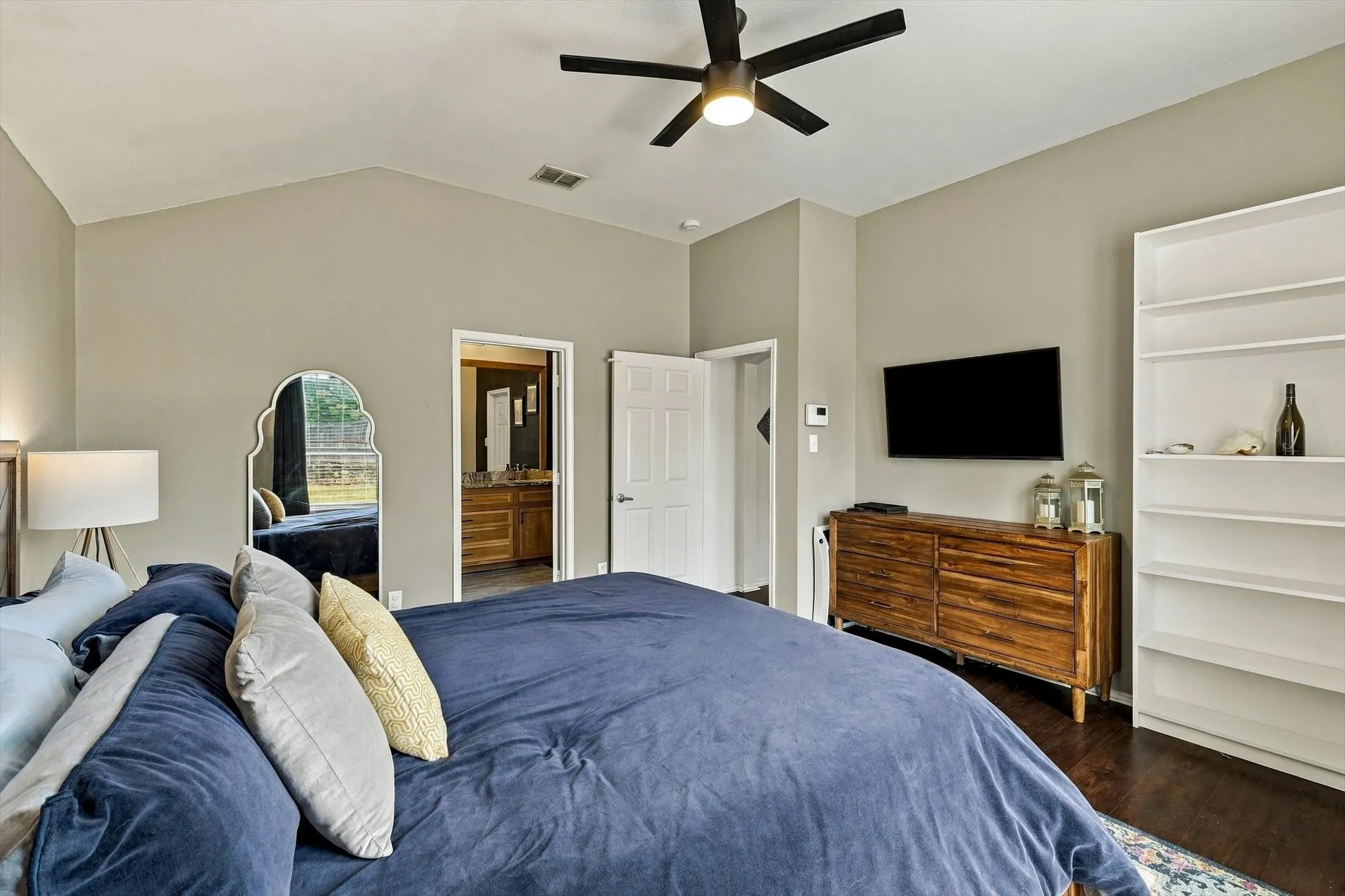 Vaulted ceiling with an attached ceiling fan, dark wood-finish flooring, and a built-in shelving unit