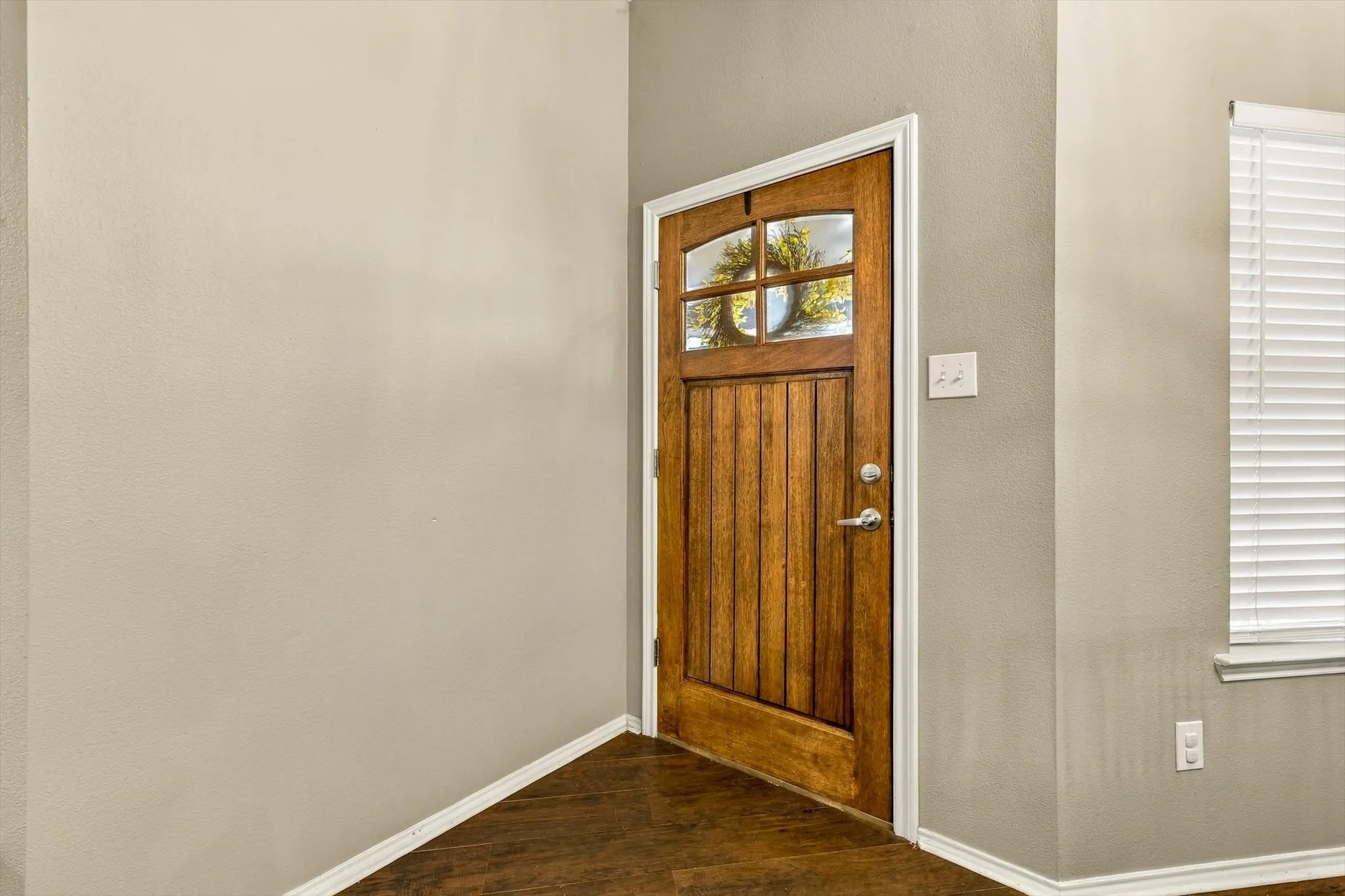 Wood-finish flooring, paneled wood door with arched glass detail, and neutral wall tones