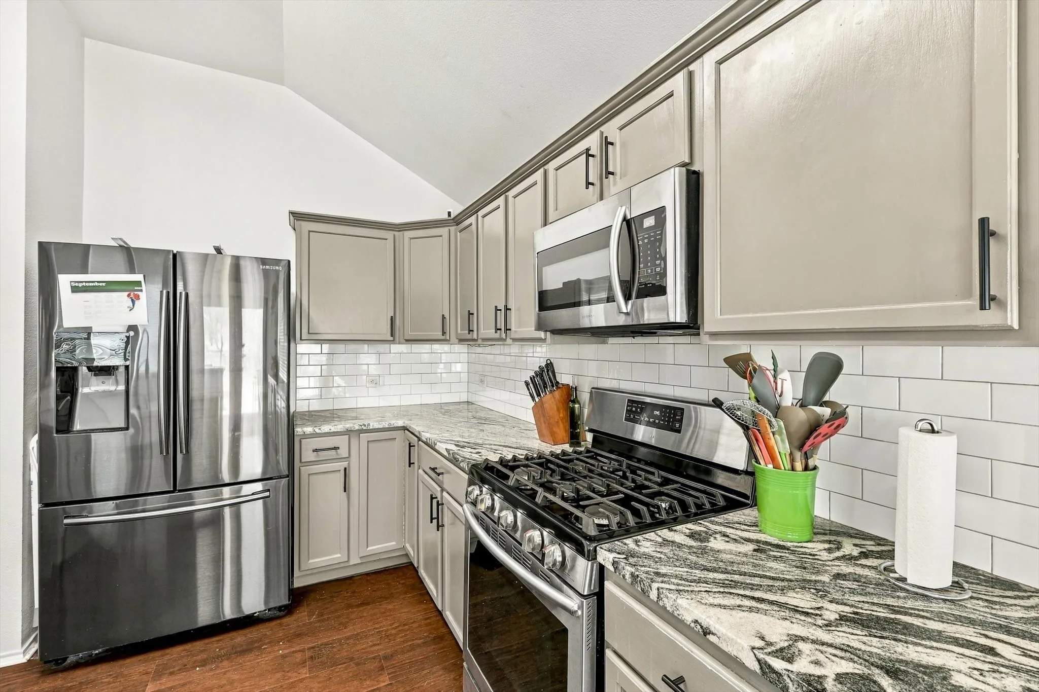 Kitchen featuring wood-finish flooring, stainless steel appliances, stone countertops, white subway tile backsplash, and light-toned cabinetry