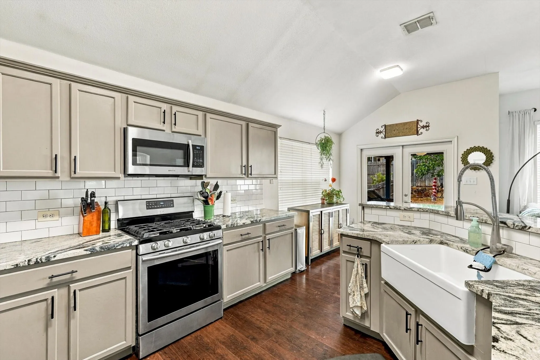 Kitchen featuring a vaulted ceiling, wood-finish flooring, white subway tile backsplash, light-toned cabinetry, and a farmhouse sink